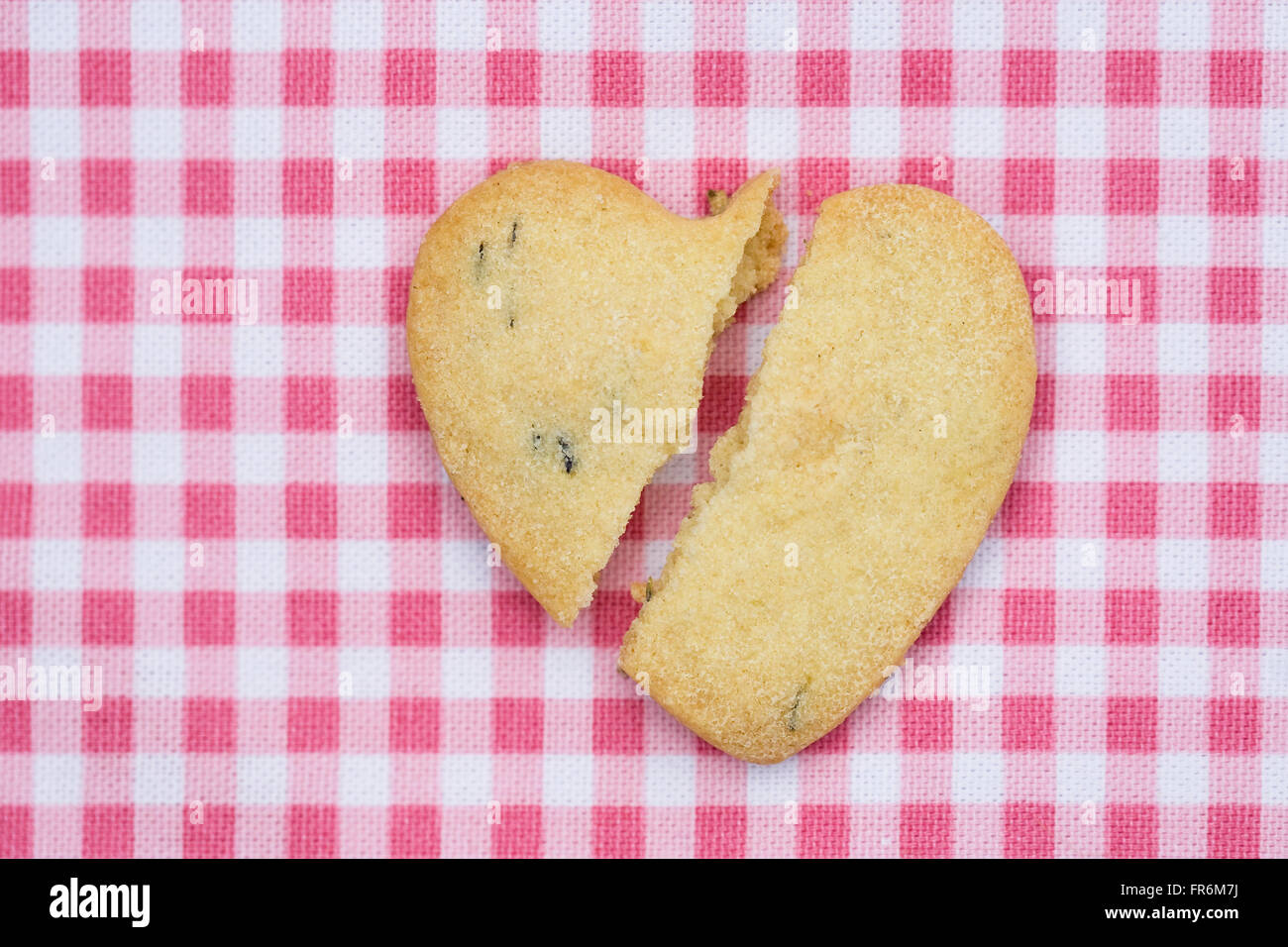 Ein gebrochenes Herz geformt Keks auf einem rosa Hintergrund geprüft. Stockfoto