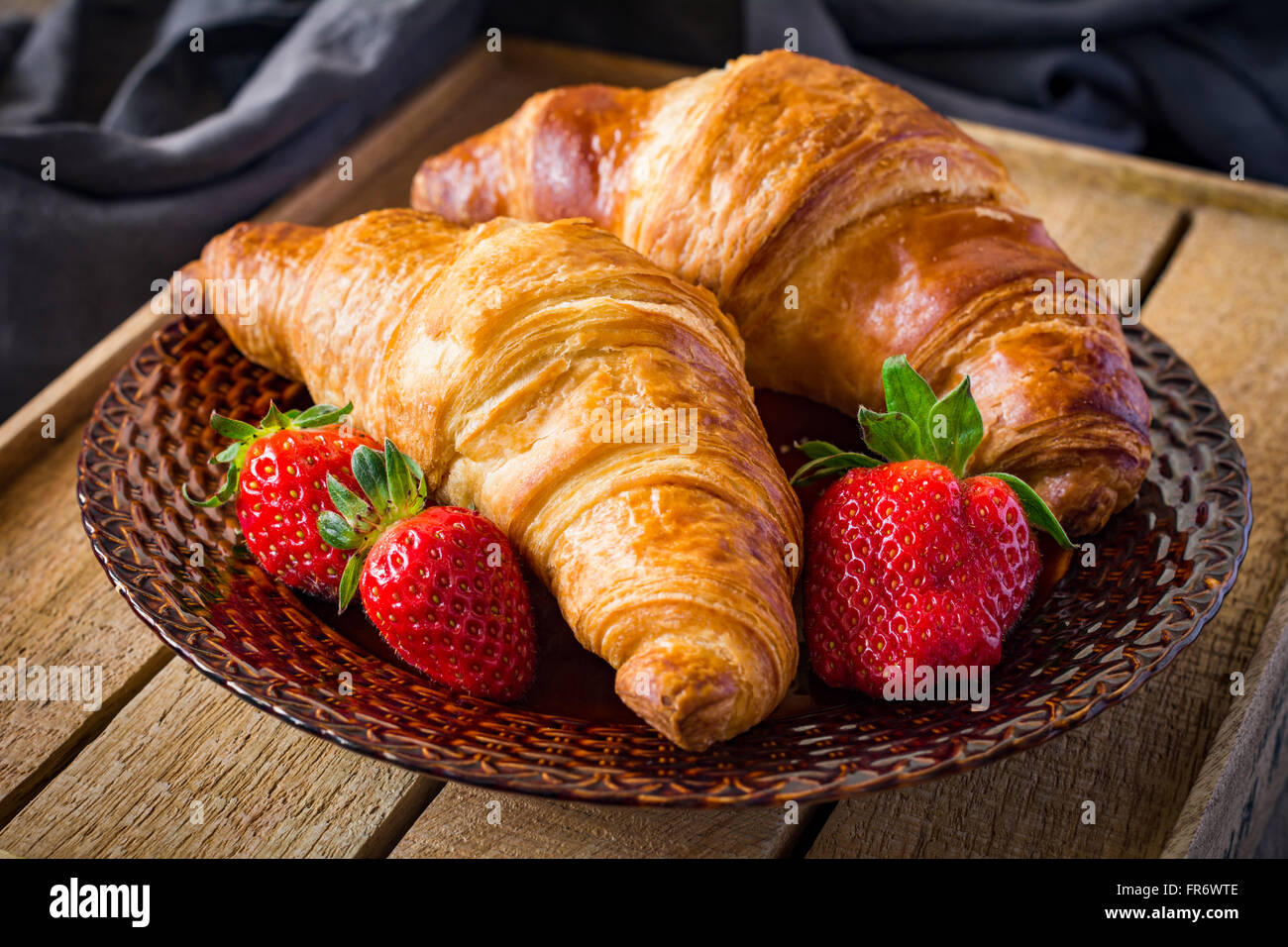 Frische Croissants mit Erdbeeren auf Teller auf hölzernen Hintergrund. Kontinentales Frühstück Essen, Warmton Stockfoto