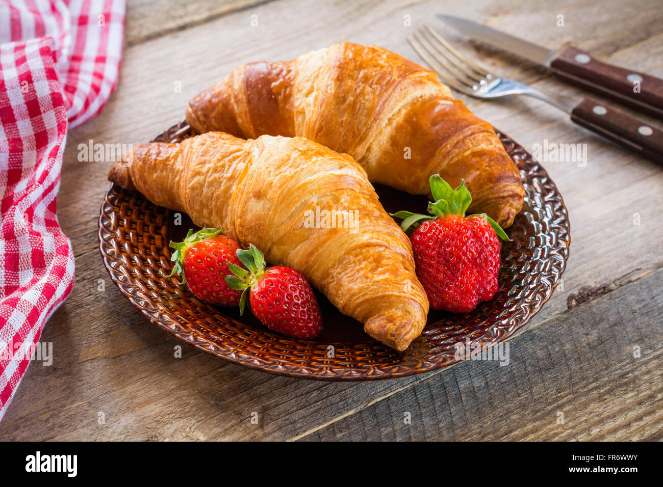Frische Croissants mit Erdbeeren auf Teller auf hölzernen Hintergrund. Kontinentales Frühstück Essen, Warmton Stockfoto