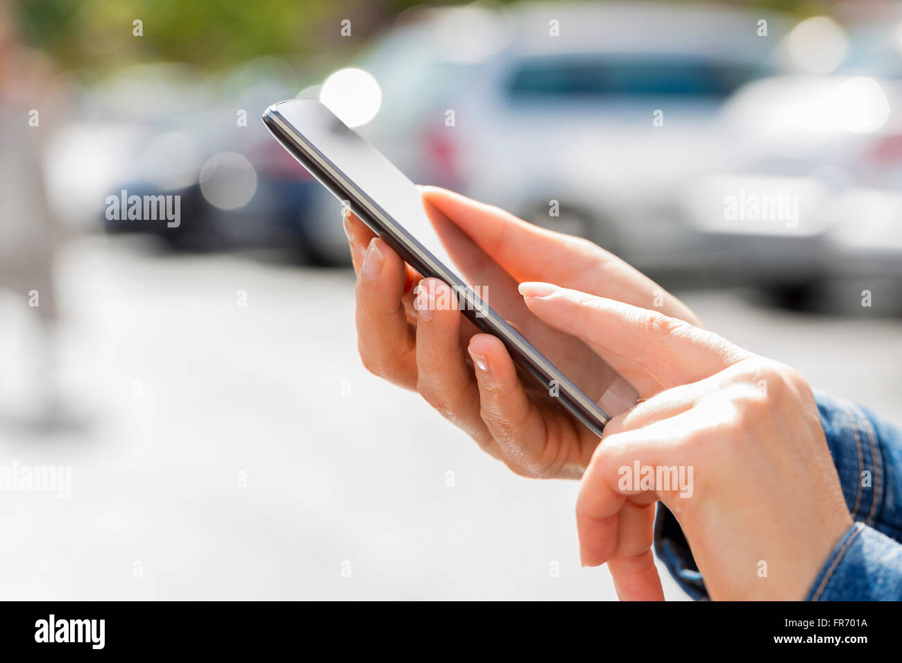 Frau auf der Suche nach ihrem Auto mit Handy im Auto Stockfoto