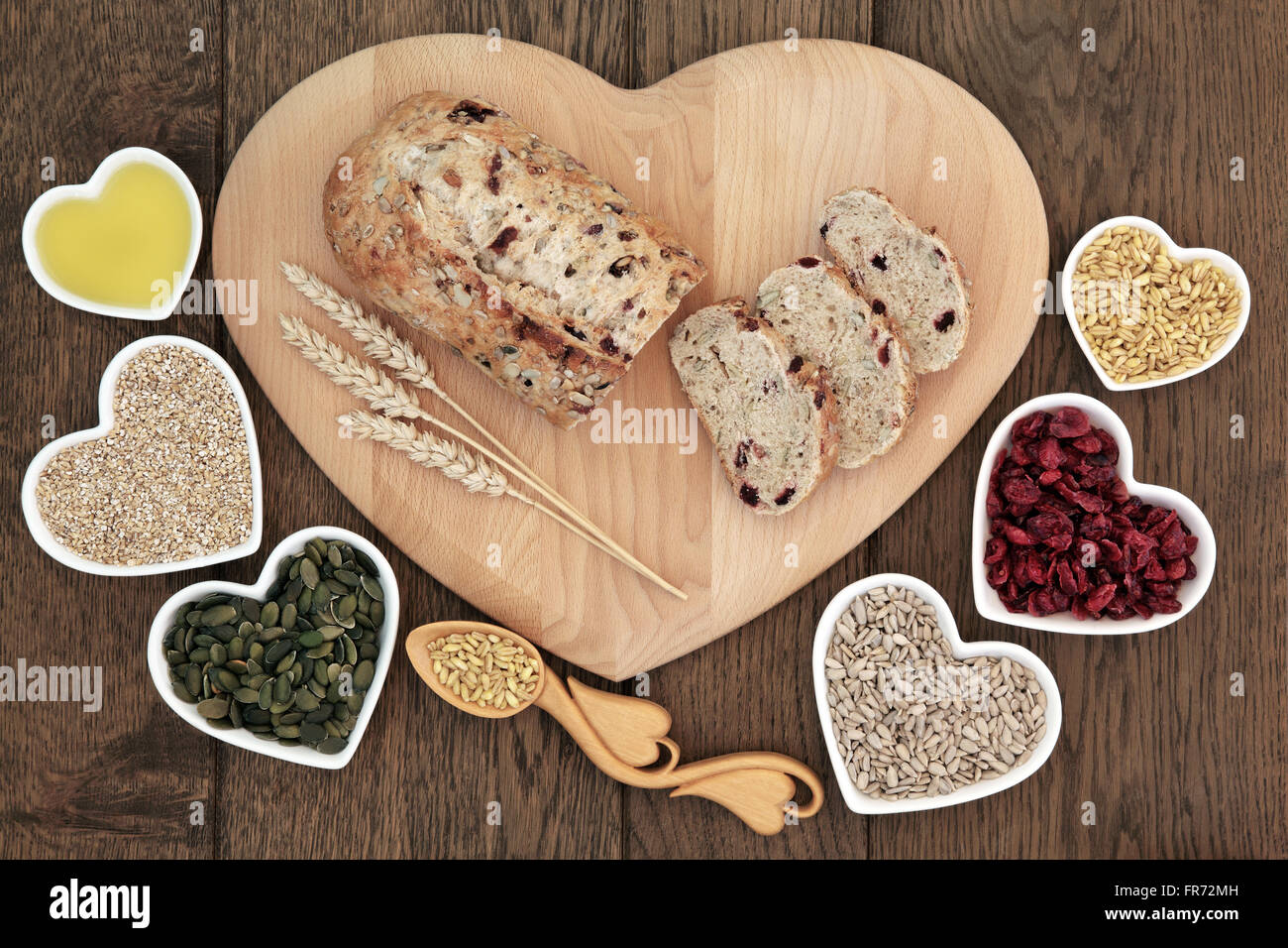 Cranberry Seed Brot Laib auf ein Holzbrett mit Weizen scheiden, Lovespoon mit Getreide, Kürbis und Sonnenblumen Samen in Herzform. Stockfoto