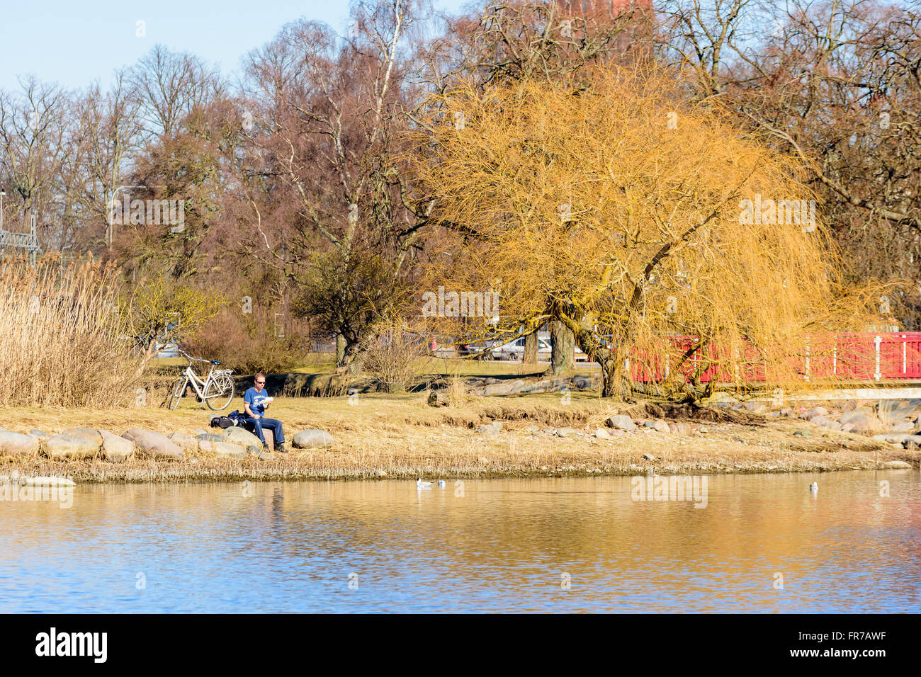Kalmar, Schweden - 17. März 2016: Männliche Person am Wasser mit einem Essen in der Hand und ein Fahrrad hinter ihm sitzen. Er ist Ruhe- und l Stockfoto