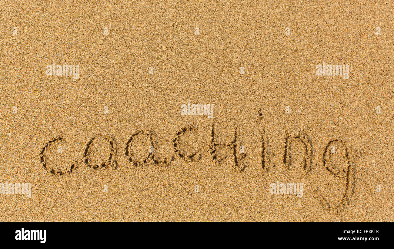 Coaching - die Inschrift auf die Textur des Meeressand. Stockfoto