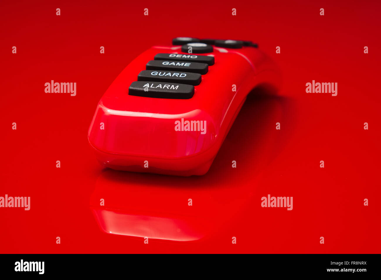 rot glänzende Fernbedienung liegen auf roten Spiegelung Oberfläche, Alarm, Wache, Spiel und Demo ist auf die Tasten aufgedruckt. Stockfoto