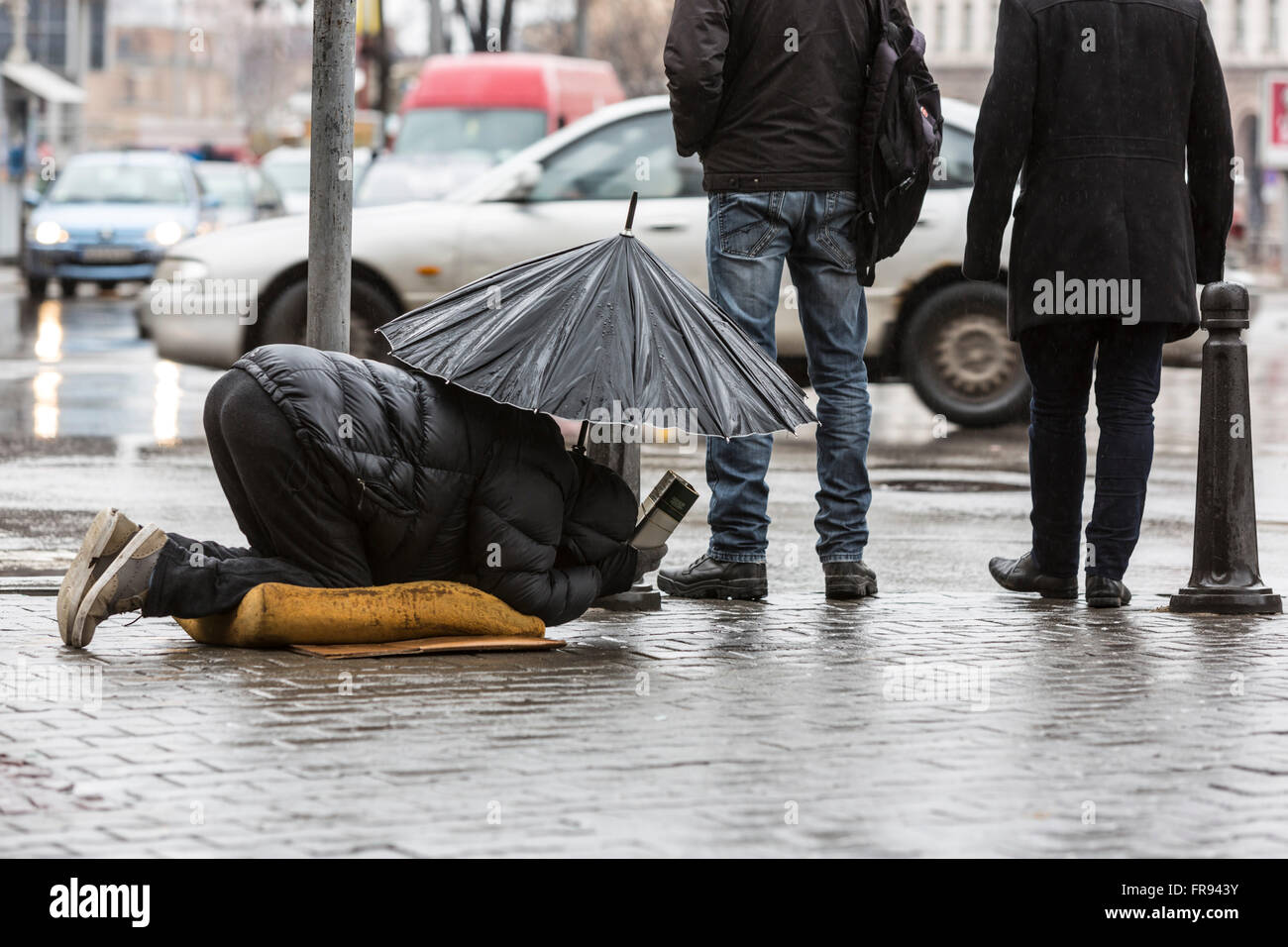 Obdachlose Bettler ist betteln um Geld in eine Hauptstraße in Sofia hält einen Regenschirm an einem regnerischen Tag. Bulgarien ist die Anzahl der ärmsten Stockfoto