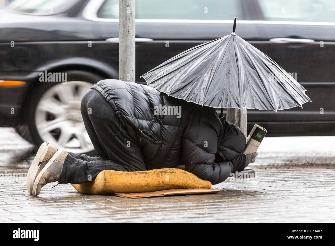 Obdachlose Bettler ist betteln um Geld in eine Hauptstraße in Sofia hält einen Regenschirm an einem regnerischen Tag. Bulgarien ist die Anzahl der ärmsten Stockfoto
