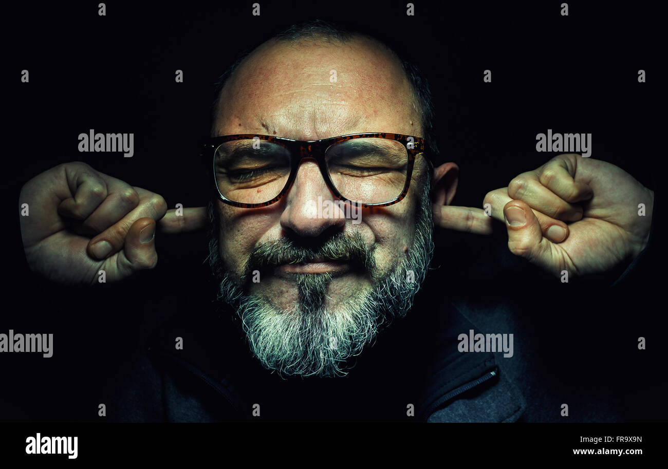 Porträt eines älteren Mannes mit Brille, mit den Fingern in den Ohren, Augen fest geschlossen. Stockfoto