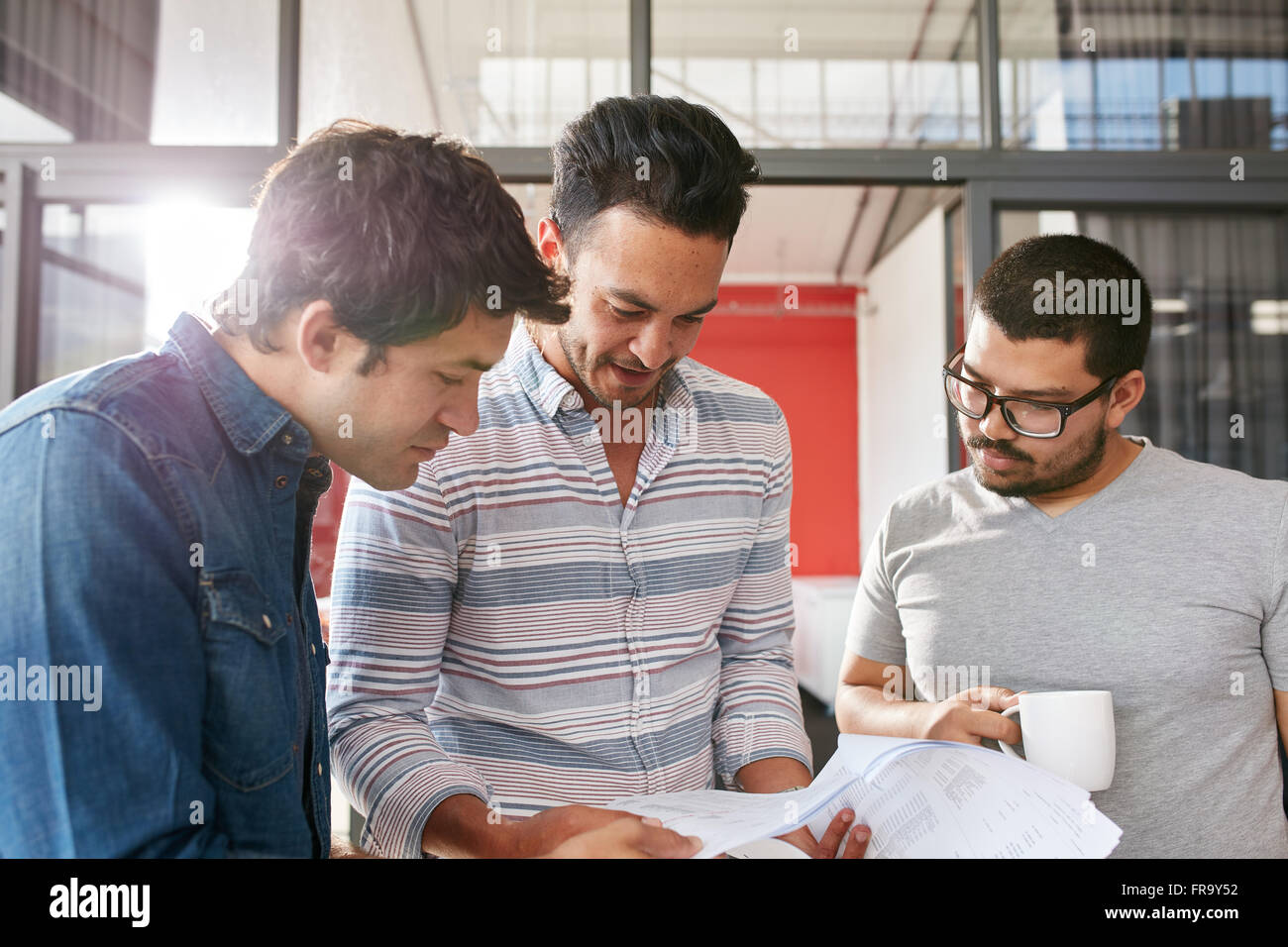 Kreativ-Team arbeitet an ihrem Geschäftsprojekt zusammen im Büro. Drei junge Männer betrachten einige Dokumente in ein kleines treffen Stockfoto