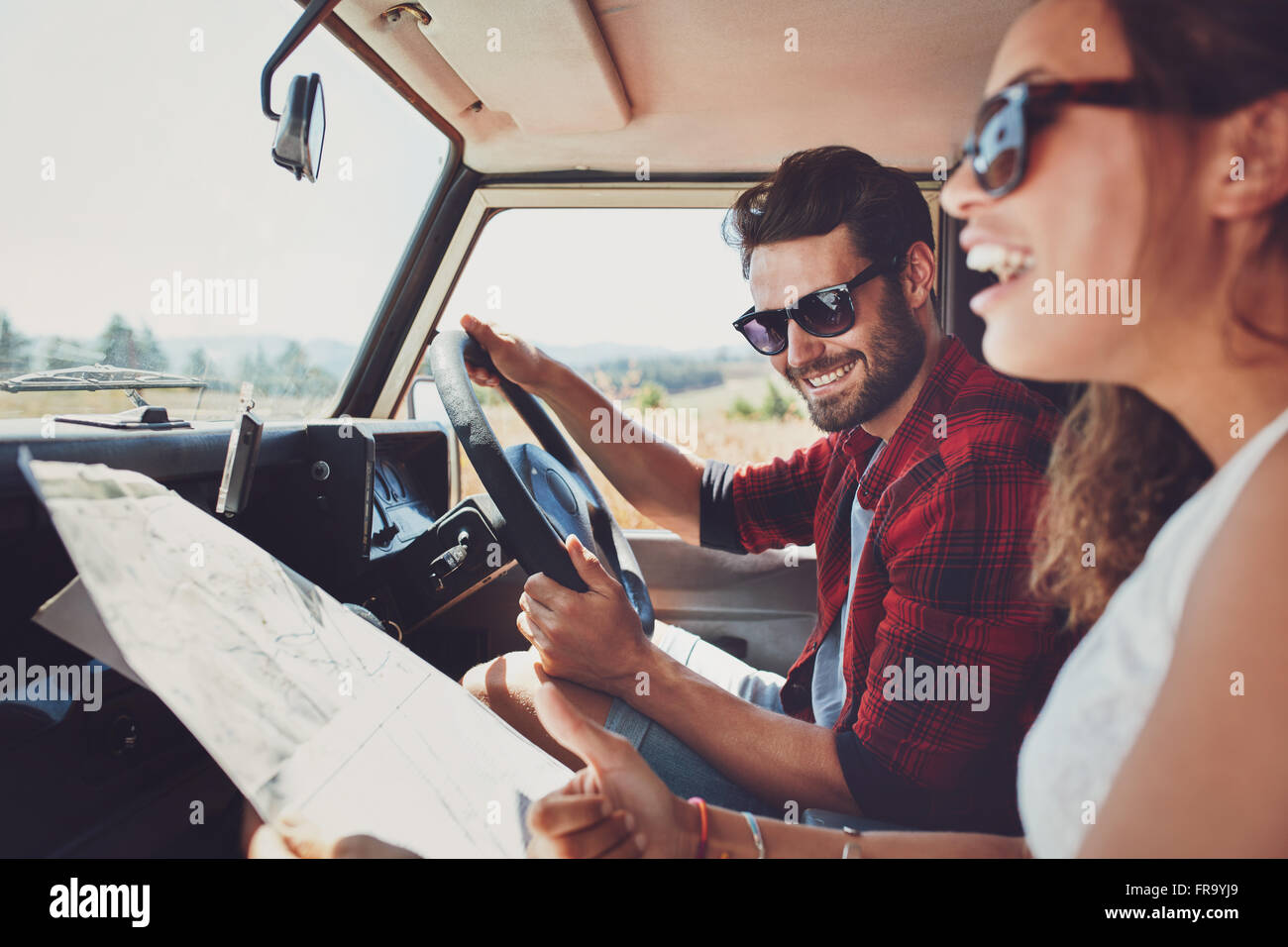 Glückliches junges Paar mit einer Karte im Auto. Lächelnder Mann und Frau mit Karte auf Roadtrip. Stockfoto