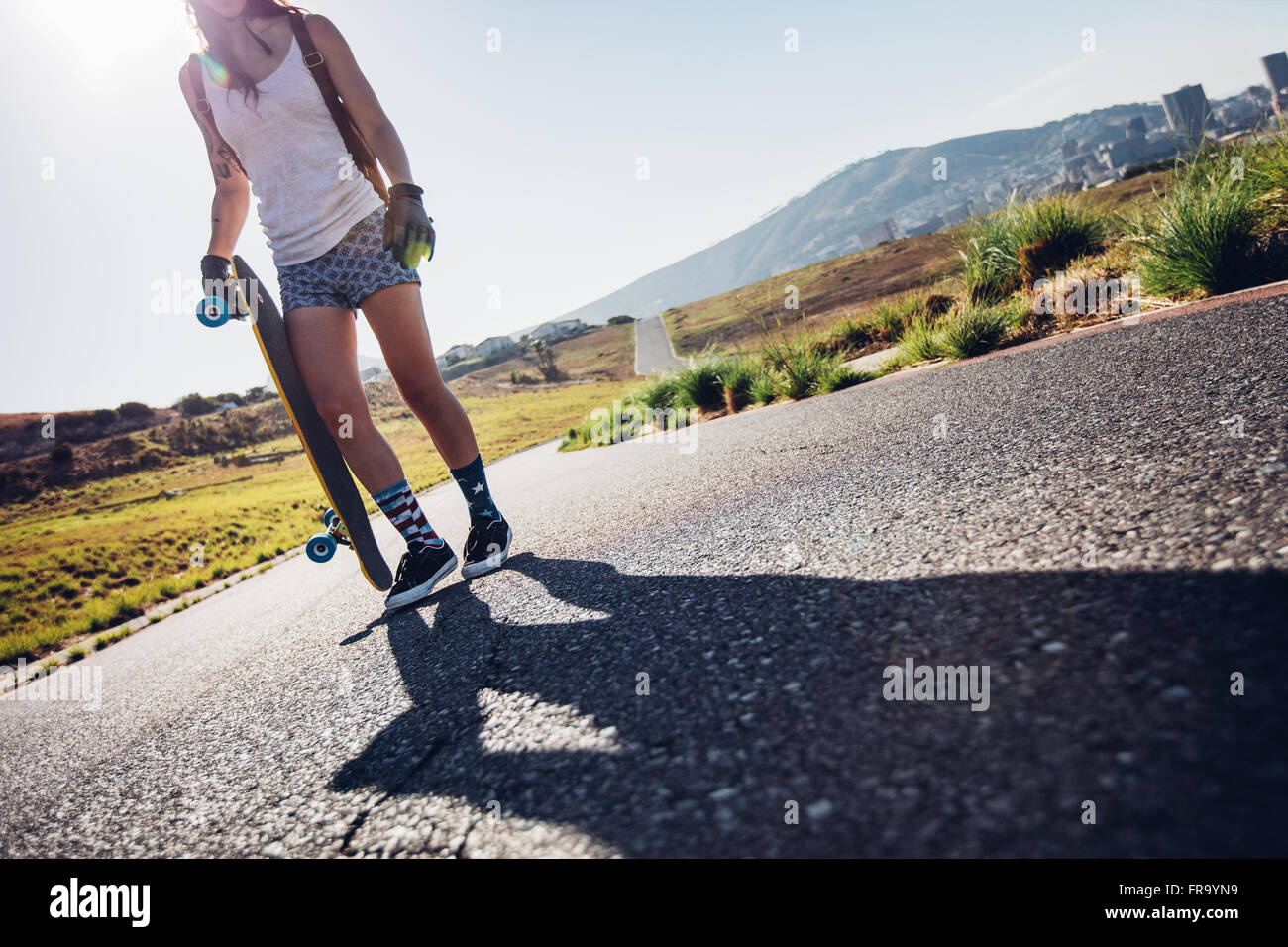 Aufnahme der jungen Frau zu Fuß mit ihrem Skateboard unterwegs beschnitten. Junge Frau mit einem Longboard an einem sonnigen Tag. Stockfoto