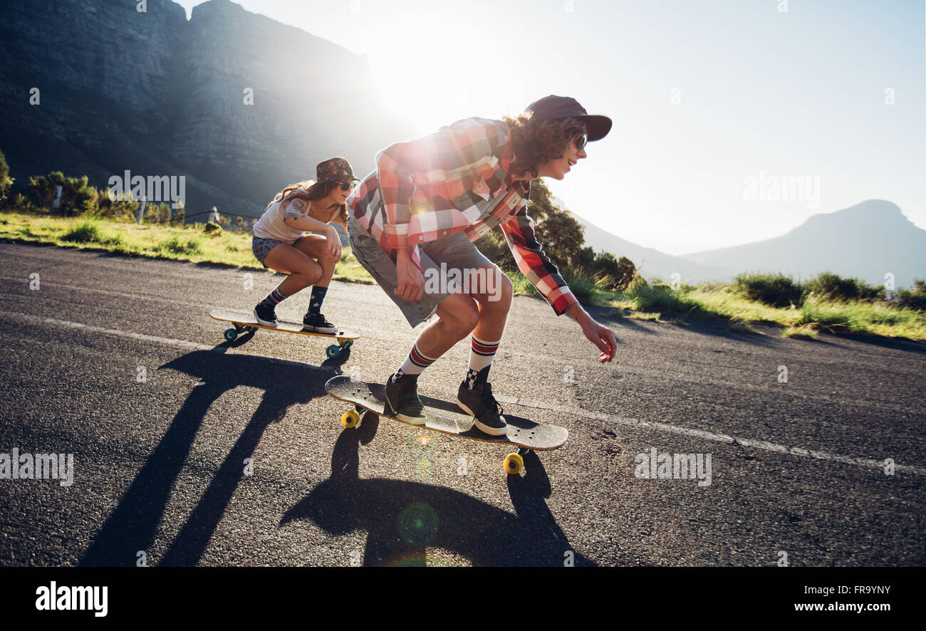Seite Porträt junger Menschen Skateboard zusammen unterwegs. Junger Mann und Frau Longboarden auf der Straße an einem sonnigen Tag. Stockfoto