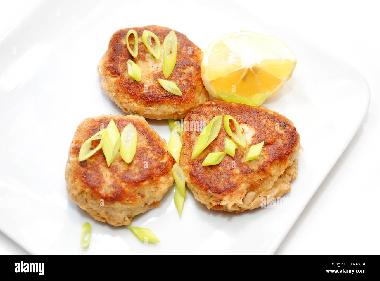 Fischfrikadellen serviert mit Zitrone und Frühlingszwiebeln Stockfoto
