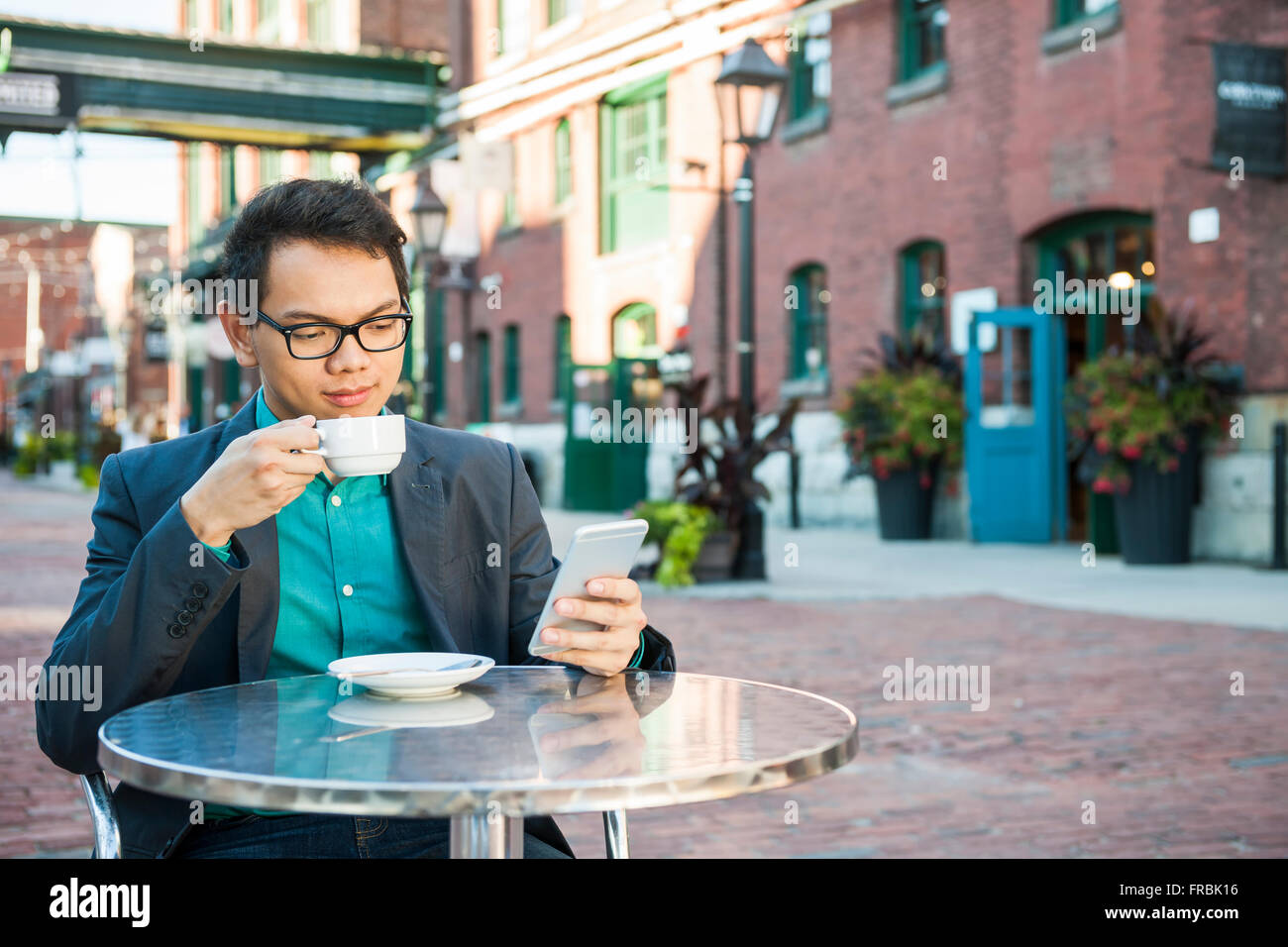 Schwere jungen asiatischen Mann in casual Geschäftskleidung sitzen in Straßencafés Tasse Kaffee zu trinken, beim Handy, mit Stockfoto