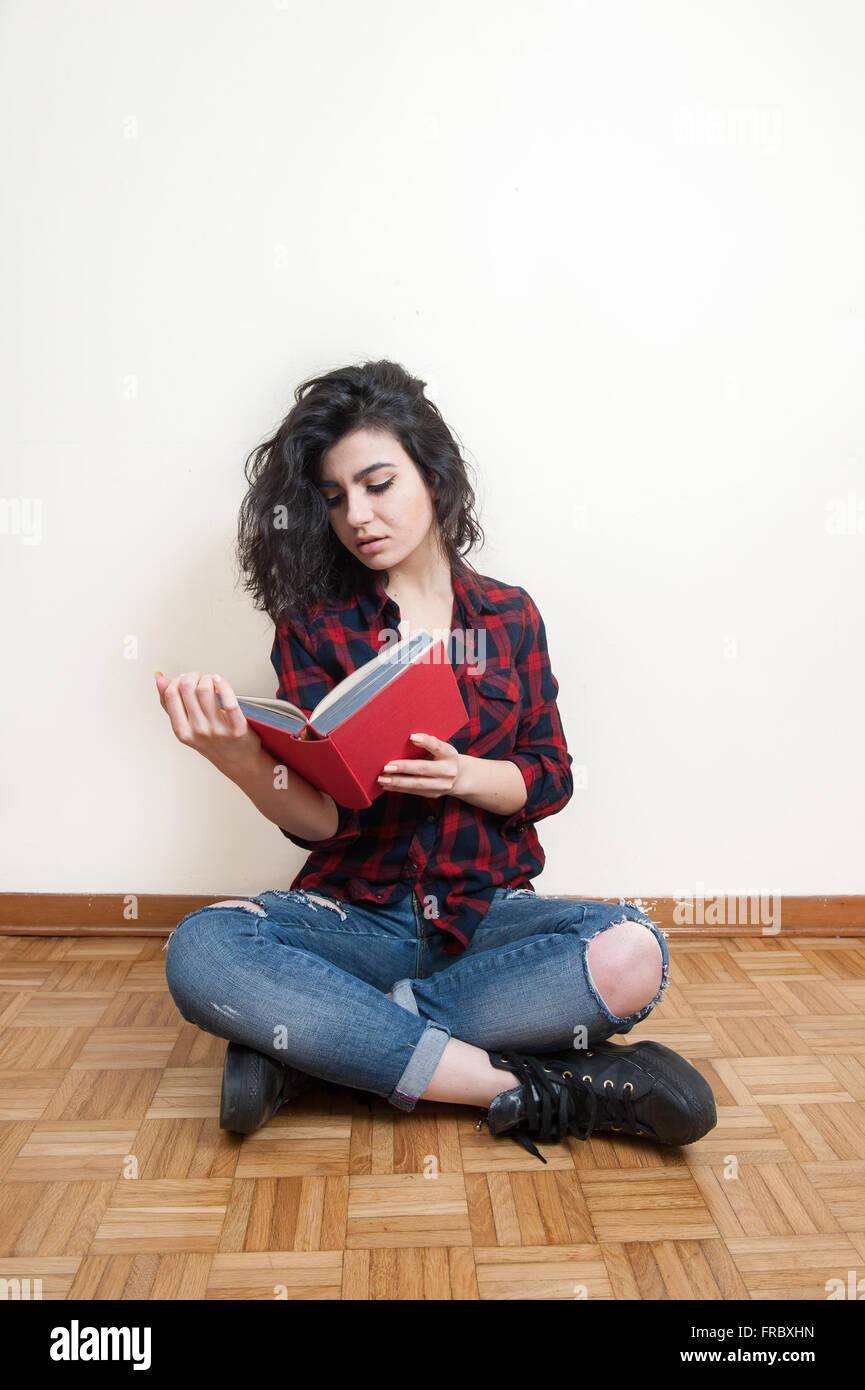 Junge Frau, die ein Buch mit rotem Einband auf dem Boden sitzend Stockfoto