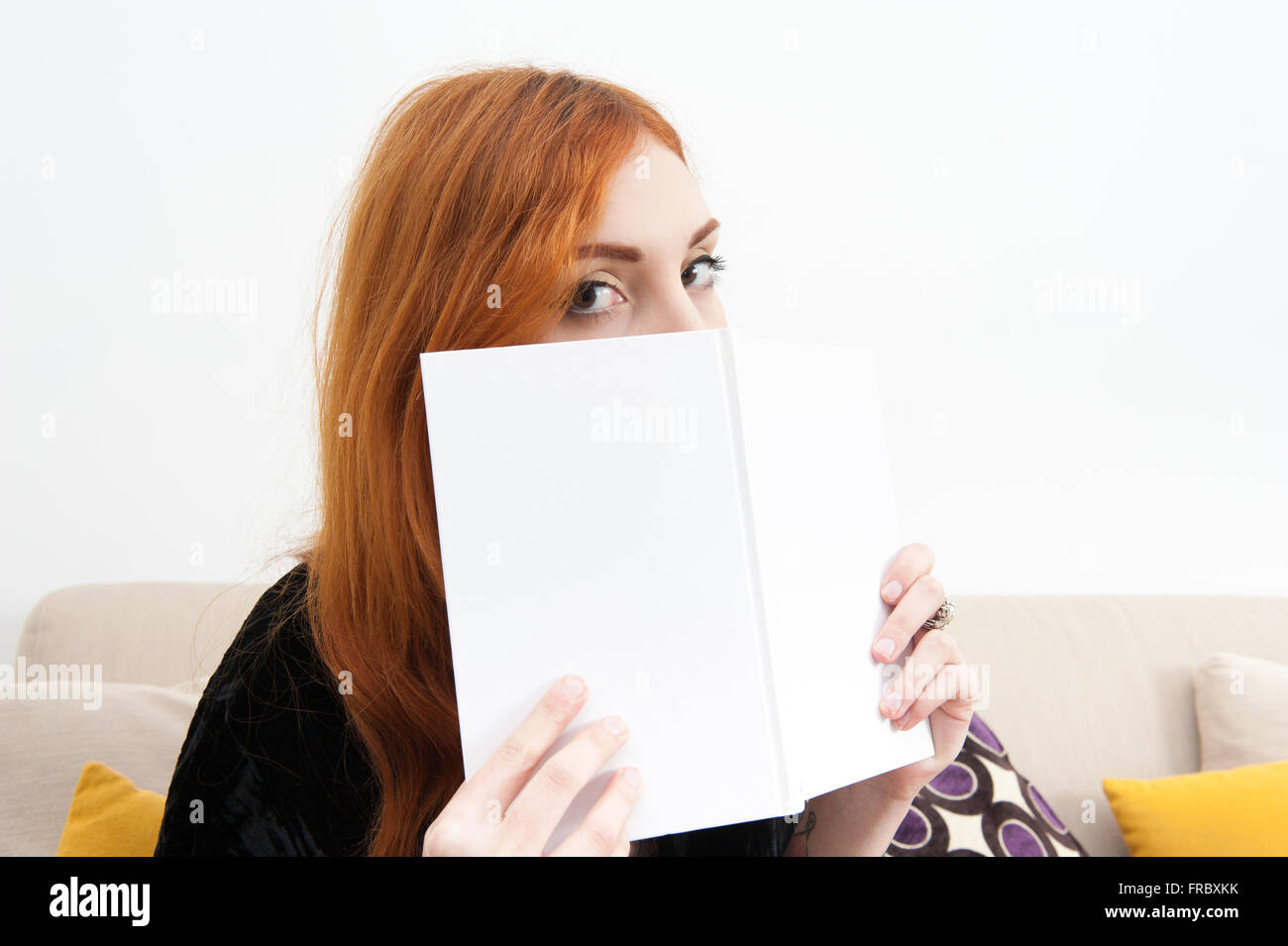 Junge rothaarige Frau zu Hause mit einem Buch, Blick in die Kamera hautnah Stockfoto