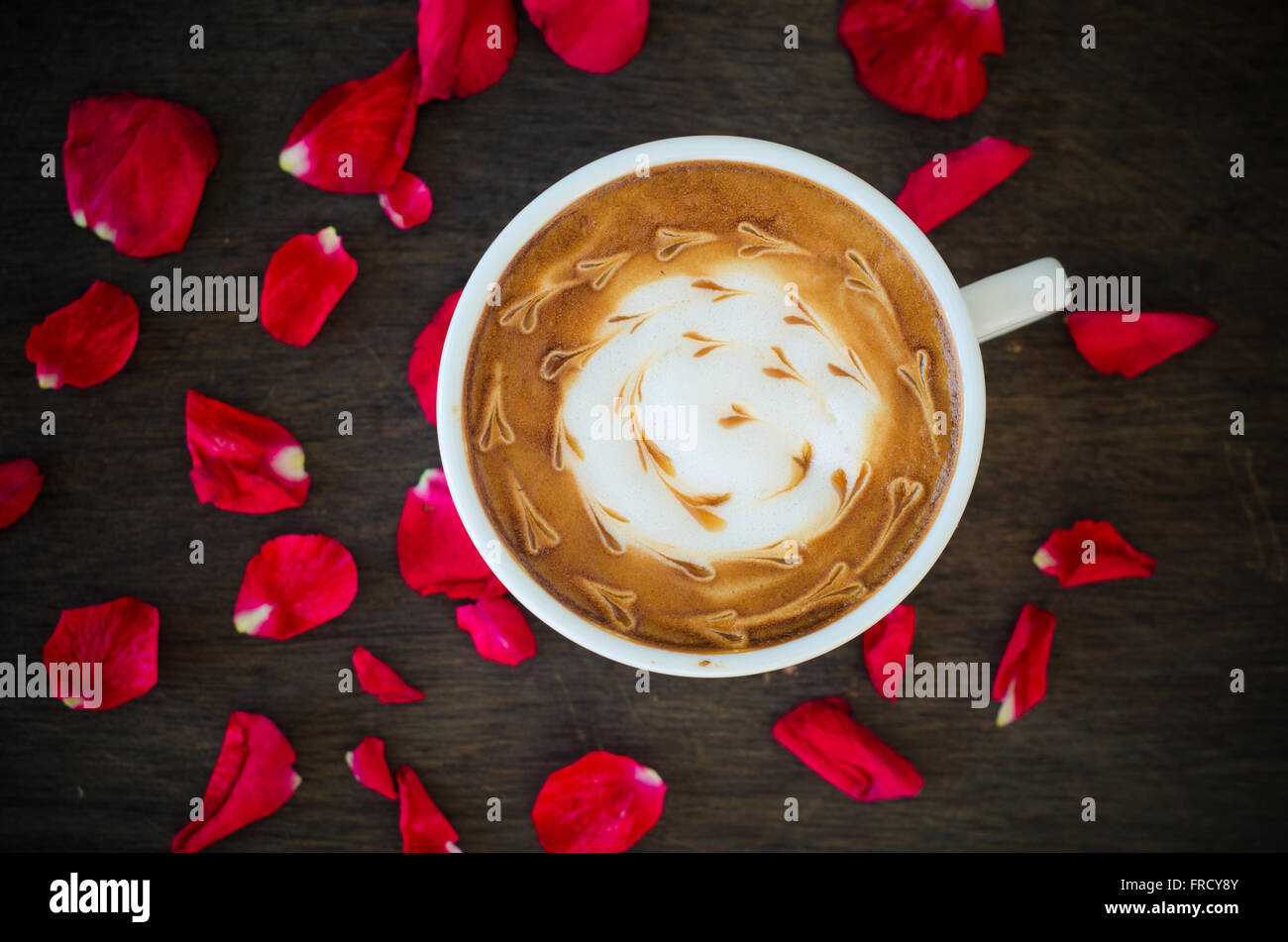 Eine Tasse Kaffee mit Latte Art und Blütenblätter stieg auf hölzernen Hintergrund Stockfoto