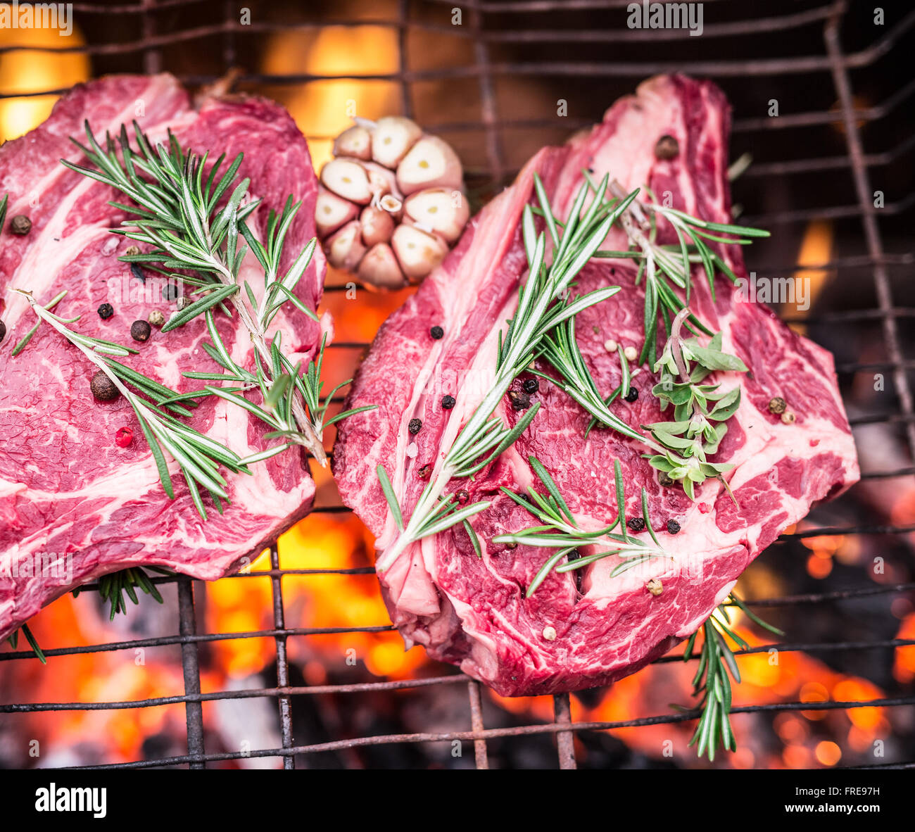 Rib-Eye-Steaks und Grill mit brennendem Feuer hinter ihnen. Stockfoto