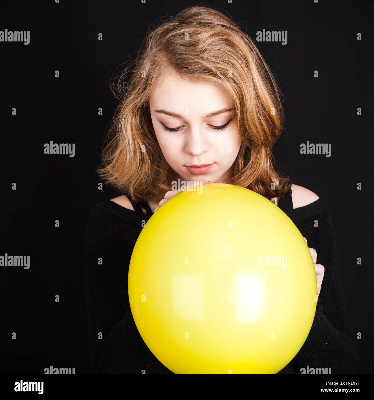 Studio-Porträt der Teenager kaukasischen blondes Mädchen mit gelben Ballon auf schwarzem Hintergrund Stockfoto