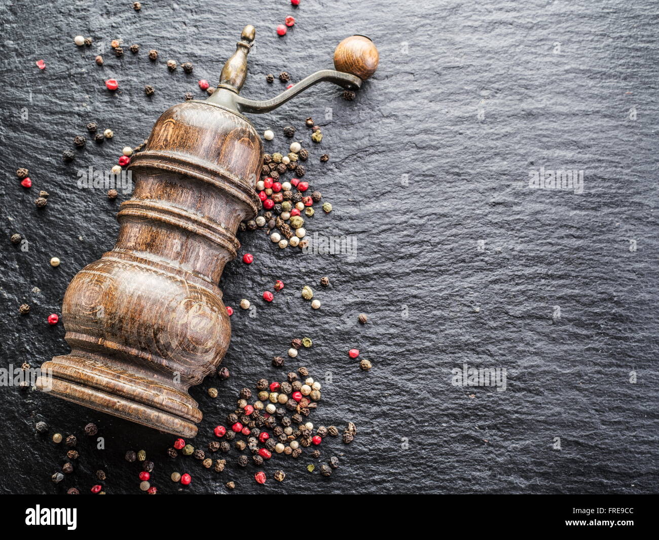 Bunte Pfefferkörner und alte Pfeffermühle auf dem schwarzen Hintergrund. Stockfoto