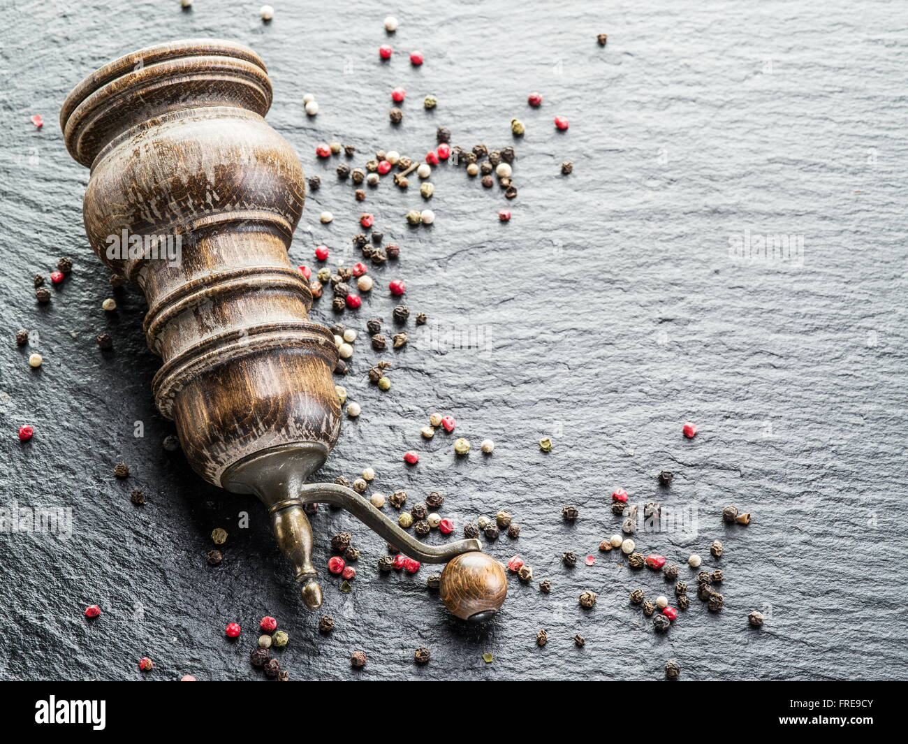 Bunte Pfefferkörner und alte Pfeffermühle auf dem schwarzen Hintergrund. Stockfoto