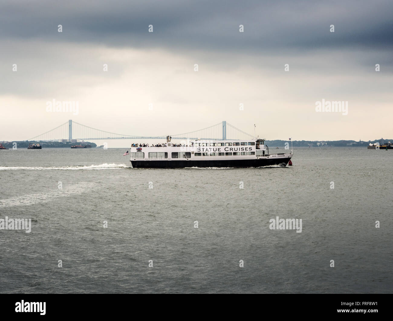 Statue Cruises Touristenboot mit Verrazano-Narrows-Brücke im Hintergrund, New York, USA. Stockfoto