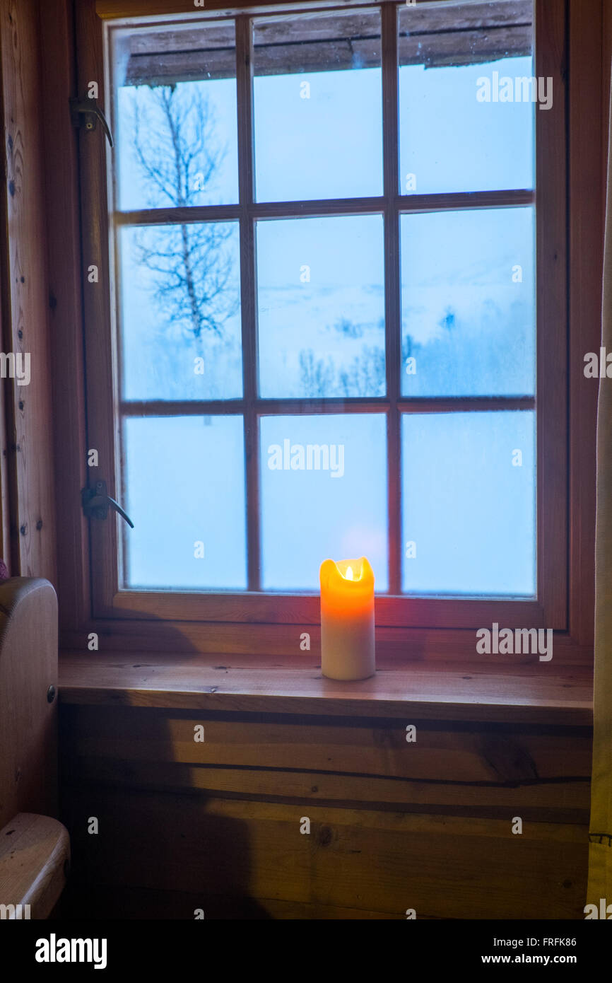 Eine Kerze im Fenster einer Hütte in den norwegischen Bergen, kaltes blaues Licht außerhalb Stockfoto