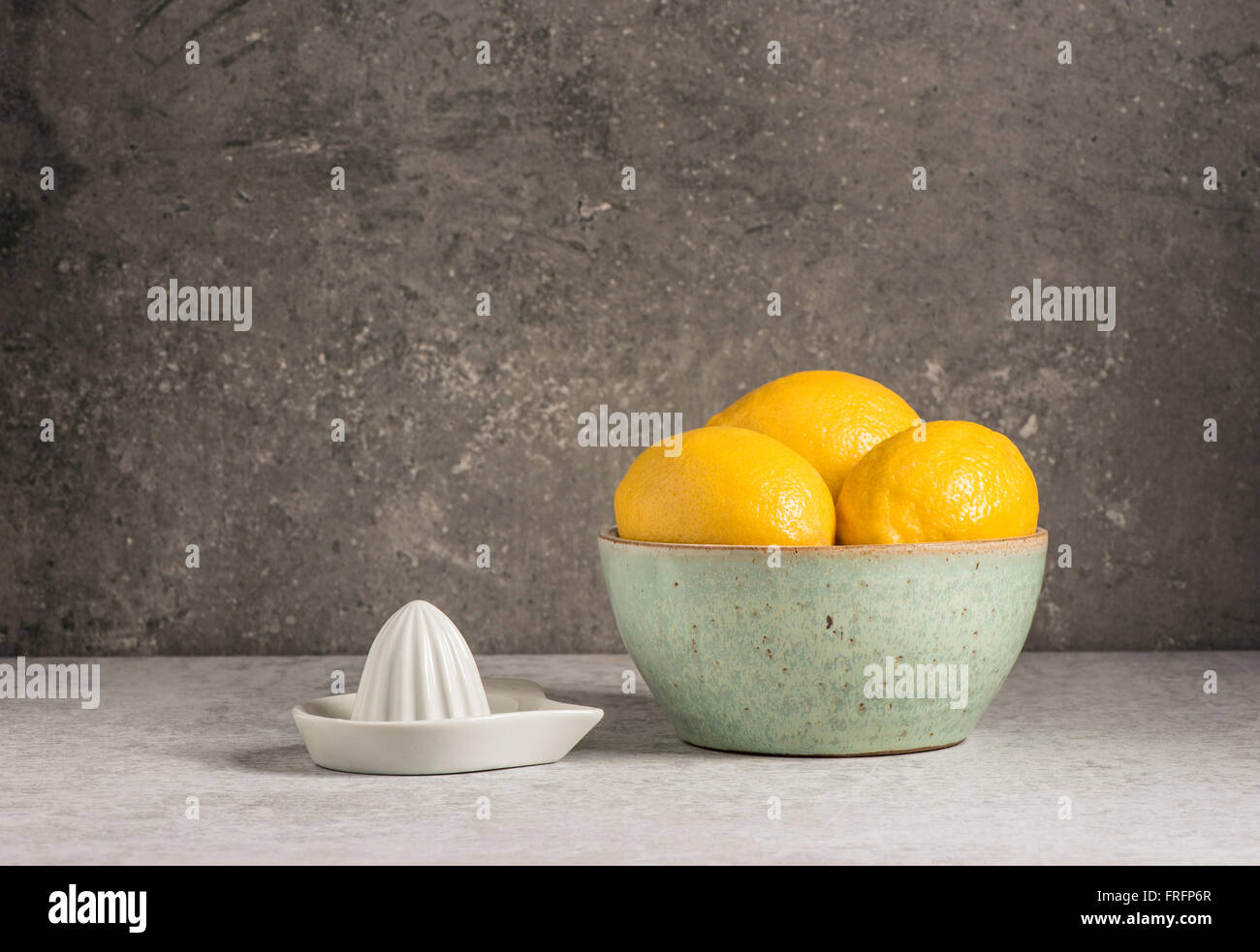 Zitronen in eine Schüssel geben und die Saftpresse am Küchentisch. Obst-Stilleben. Stockfoto