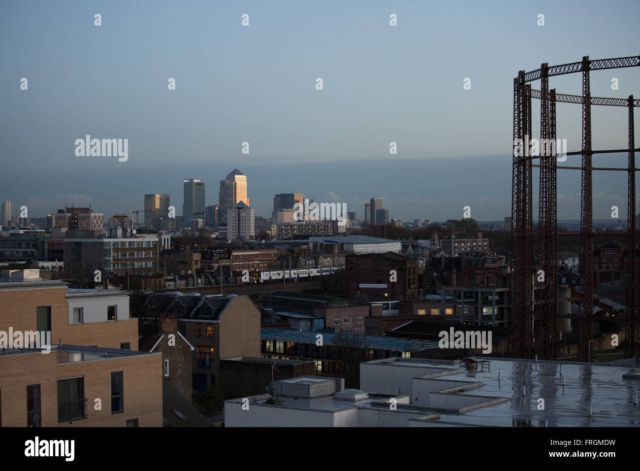 Canary Wharf Finanzviertel von Hackney in der Dämmerung zu sehen. Im Vordergrund steht eine leere Gasspeicher mit einem Zug vorbei. Stockfoto