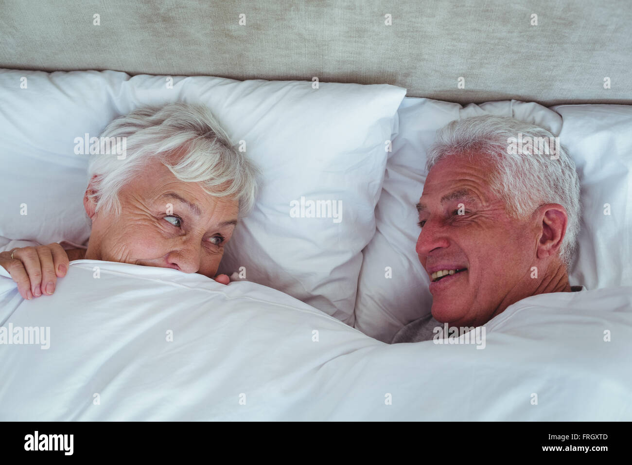 Gerne älteres paar sahen einander liegend auf Bett Stockfoto
