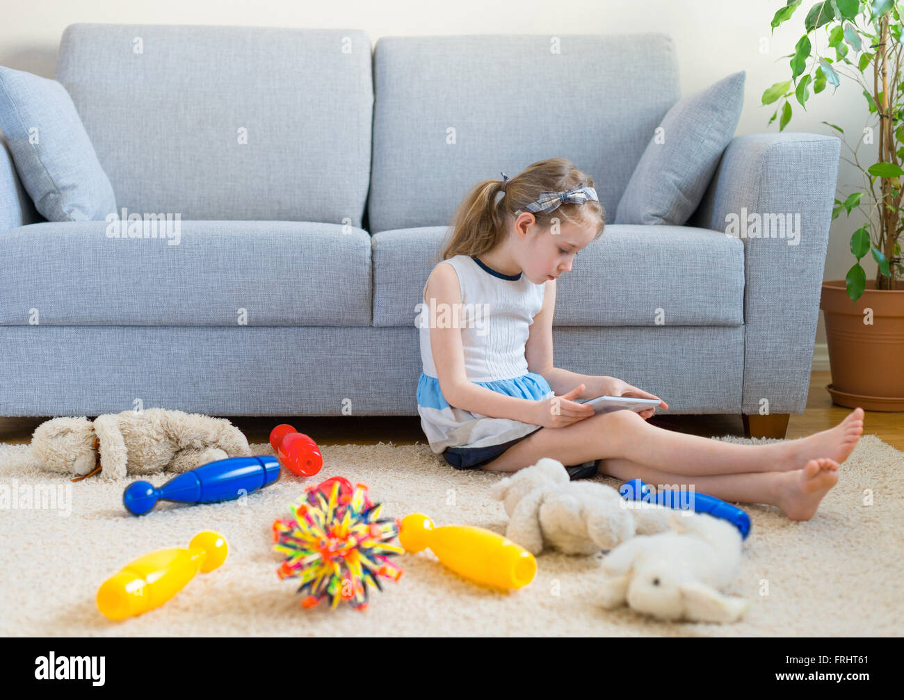Es ist Zeit, um Ihre Spielzeuge zu bereinigen! Kleine Mädchen spielen mit Tablet-pc, wollen nicht die Reinigung zu tun. Stockfoto