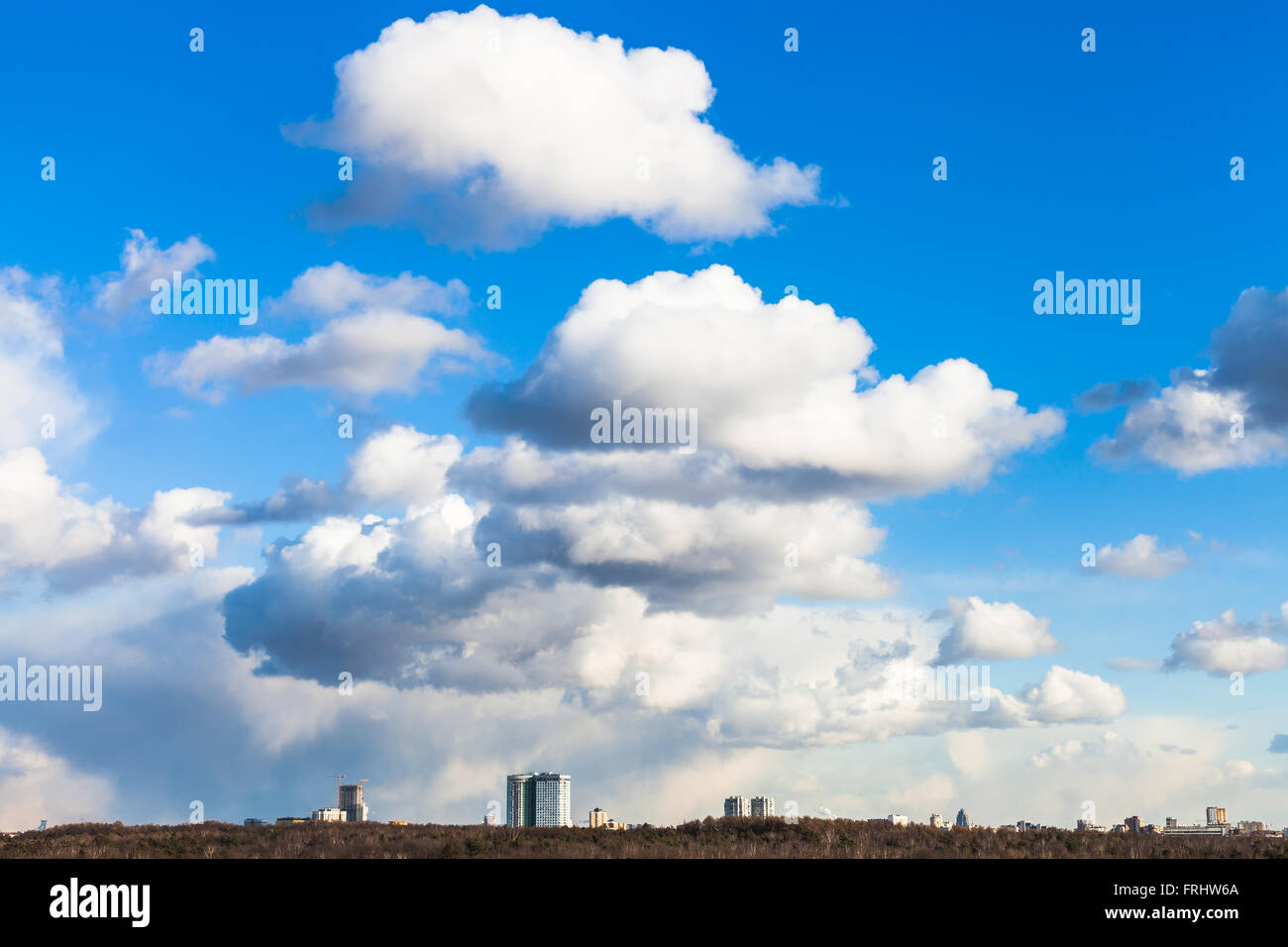 großen weißen Cumulus-Wolken am blauen Himmel über Stadthäuser und Wald im sonnigen Frühlingstag Stockfoto