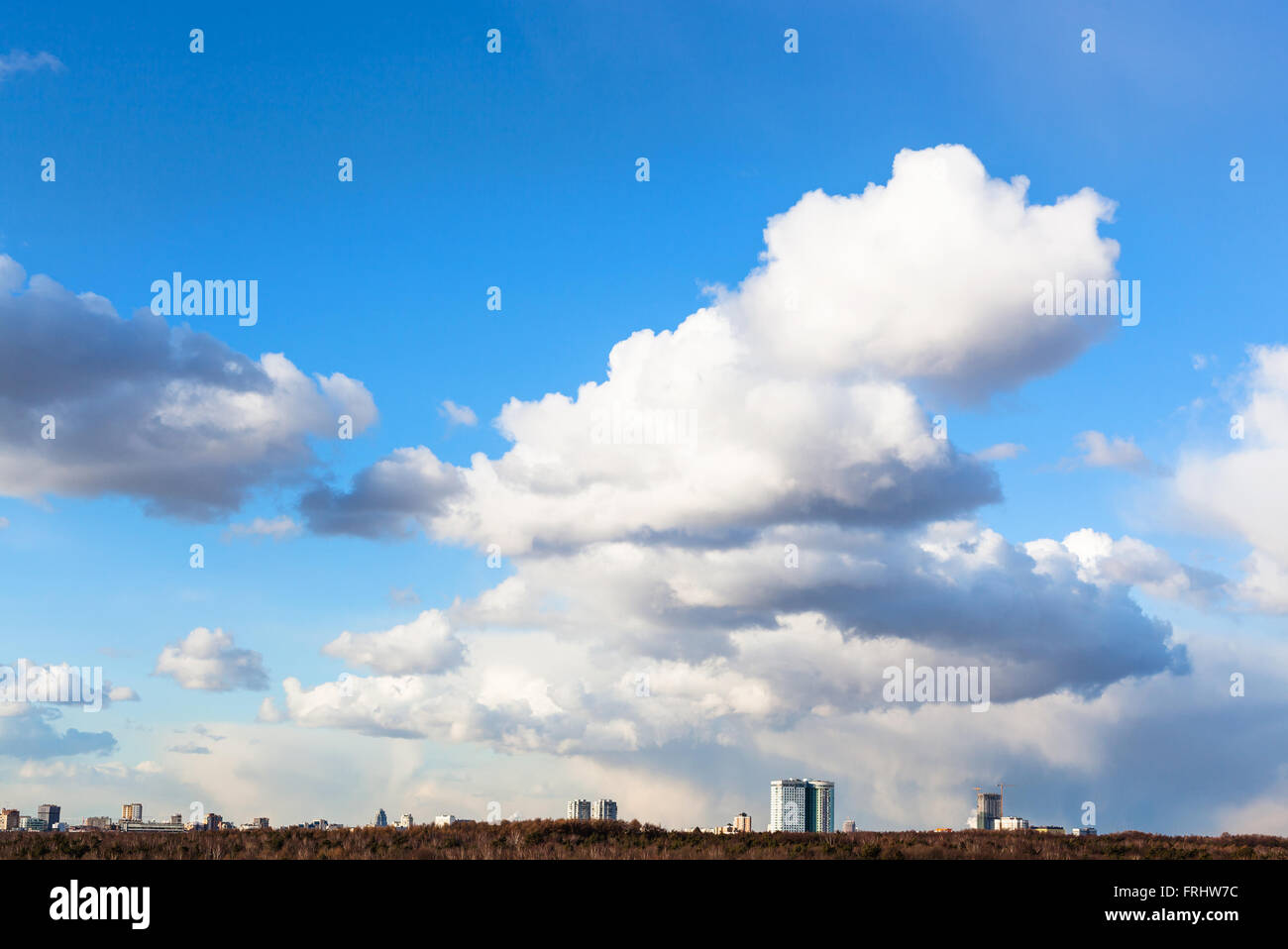 großen weißen Cumulus-Wolken am blauen Himmel über Wohnhäuser und Wald im sonnigen Frühlingstag Stockfoto
