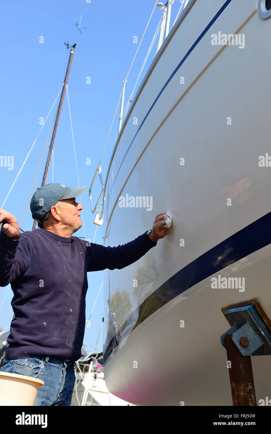 Der Bootsbesitzer poliert zu Beginn der Segelsaison den Rumpf seines Bootes an Land im Jachthafen - Chichester, West Sussex, England, Großbritannien Stockfoto