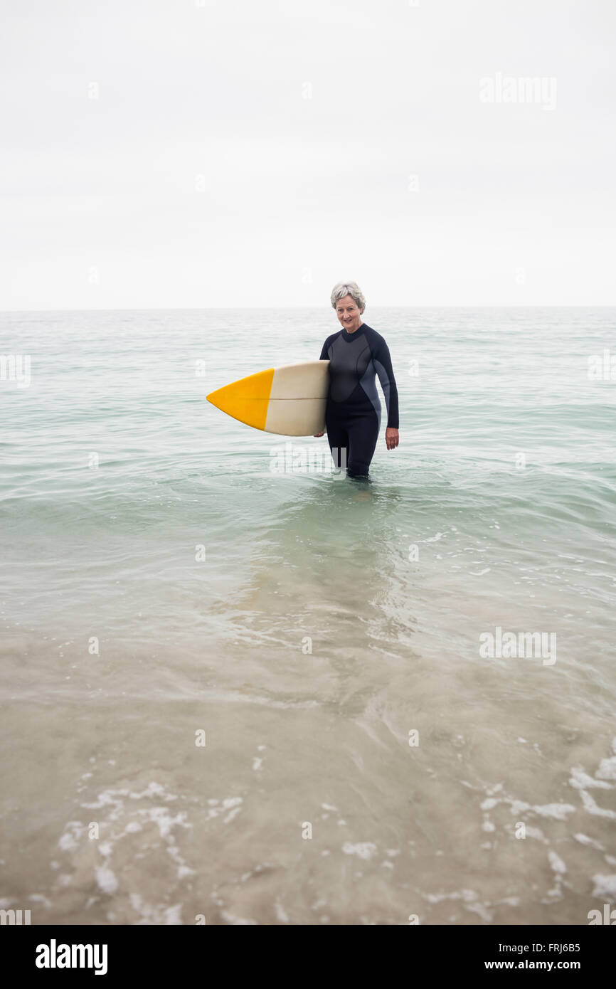 Ältere Frau im Neoprenanzug stehen im Wasser mit Surfbrett am Strand Stockfoto