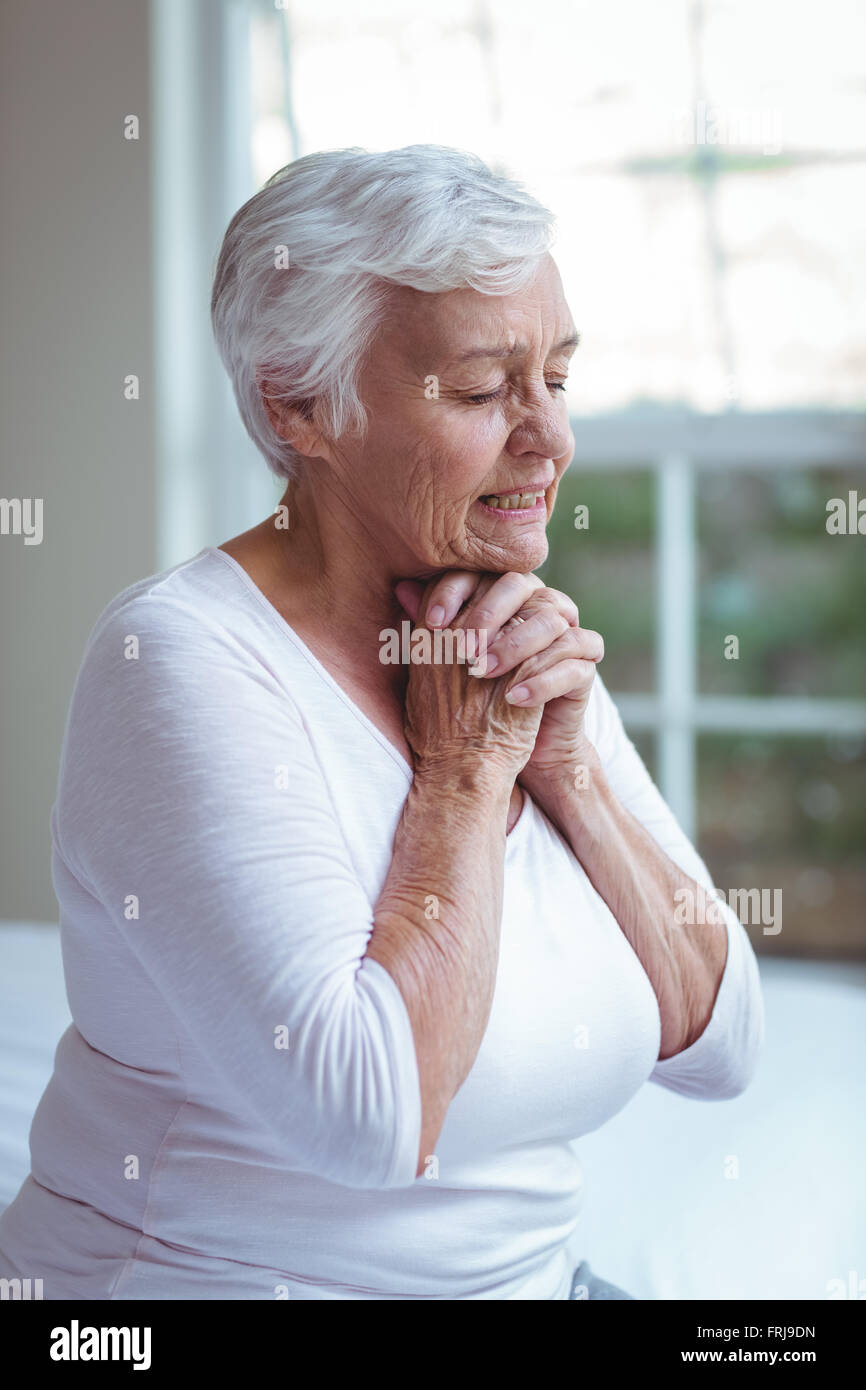 Ältere Frau beten zu Hause gegen Fenster Stockfoto