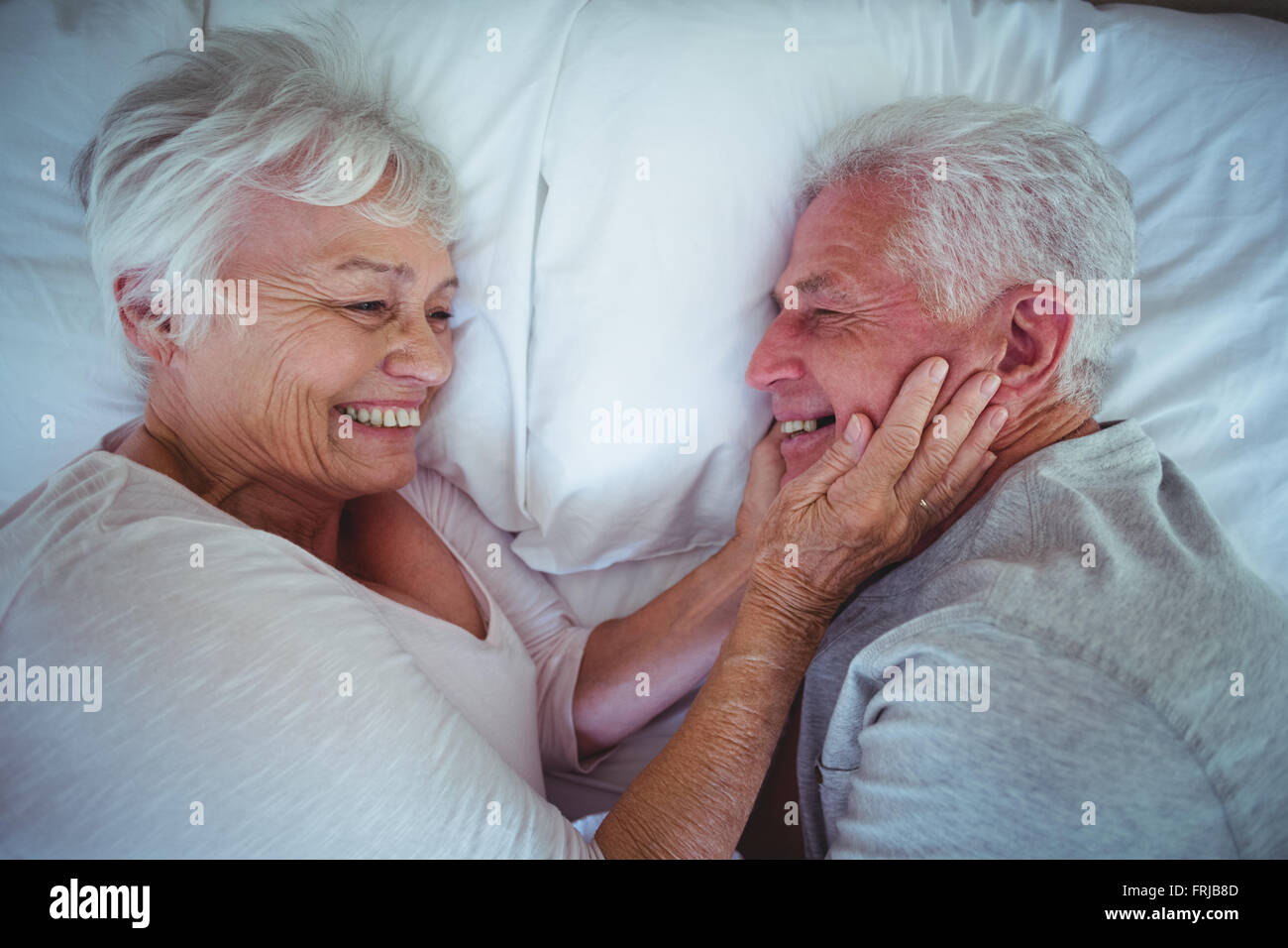 Ältere Frau mit Mann Wangen beim liegen auf dem Bett Stockfoto