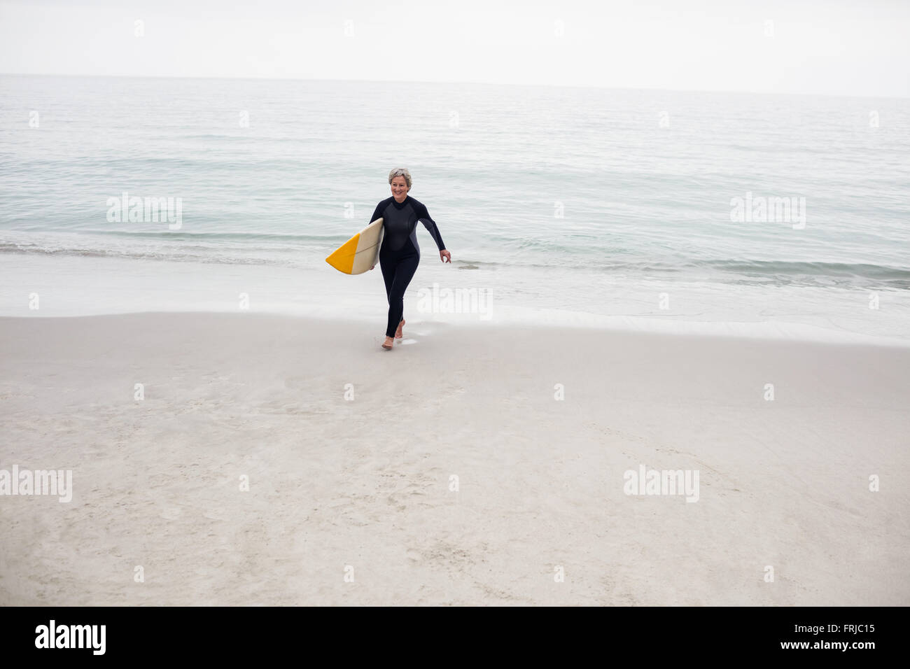 Ältere Frau zu Fuß am Strand mit einem Surfbrett Stockfoto
