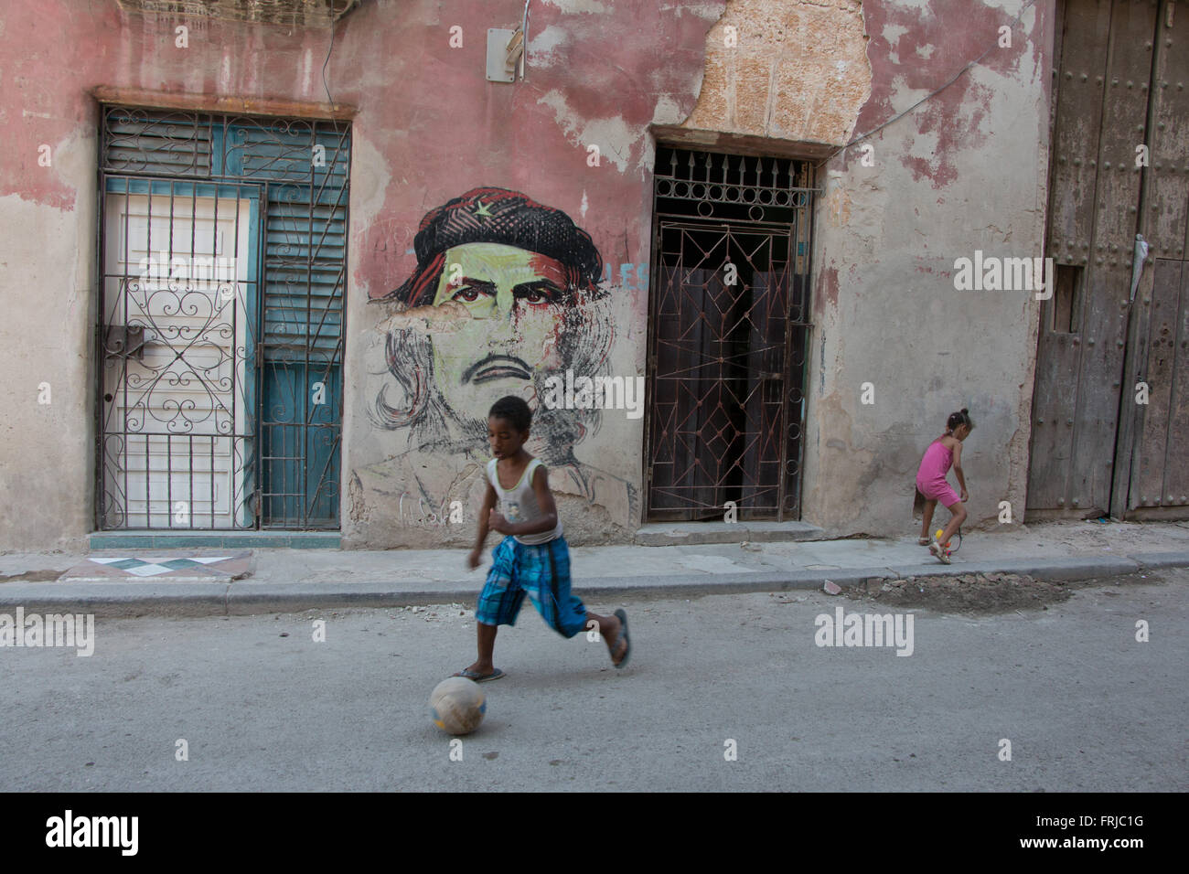 Kinder spielen in Alt-Havanna vor einer verblichenen Che Guevara Malerei Stockfoto
