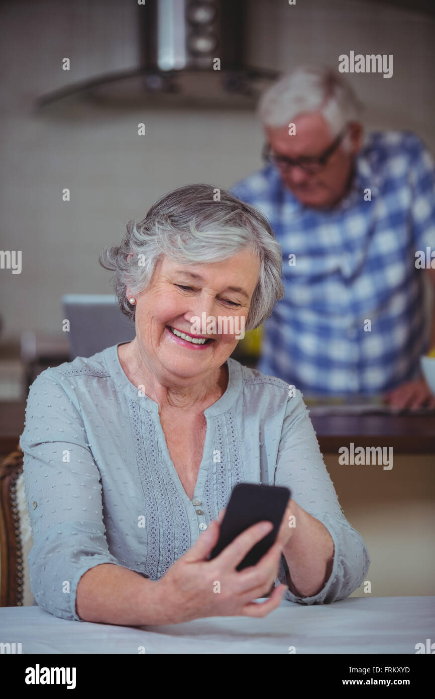 Ältere Frau mit Telefon sitzen in Küche Stockfoto