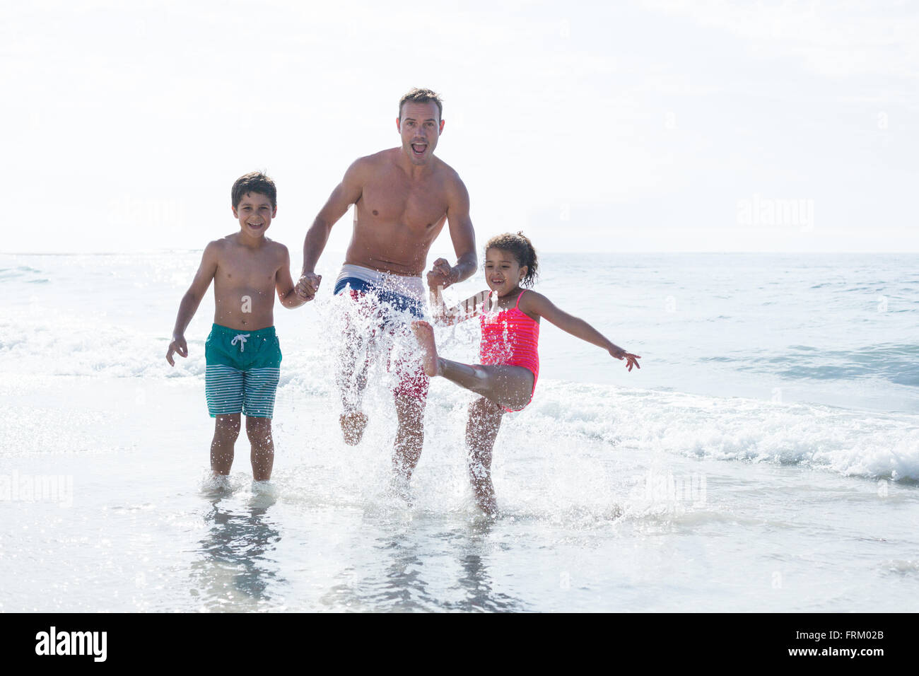 Fröhliche Vater mit Kindern im flachen Wasser genießen Stockfoto