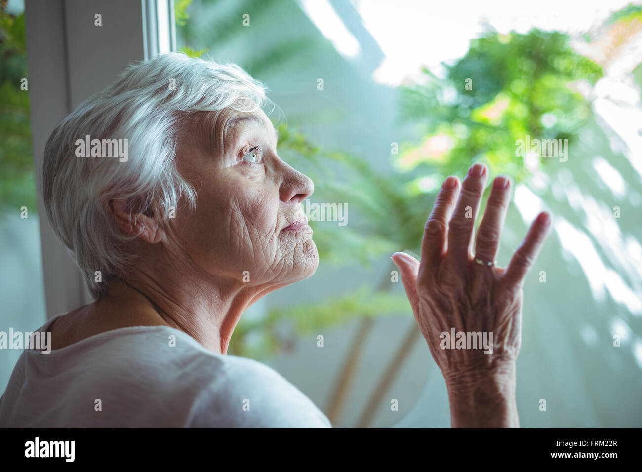 Ältere Frau, die auf der Suche durch Haus Fenster Stockfoto