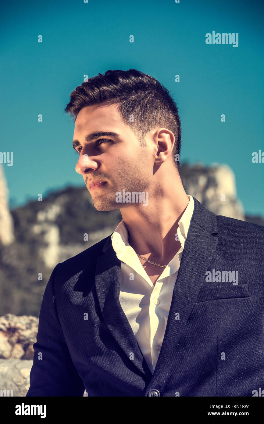 Schönen jungen Mann im klassischen Anzug am Strand halten Sonnenbrille beim wegschauen. Wellen des Meeres im Hintergrund Stockfoto