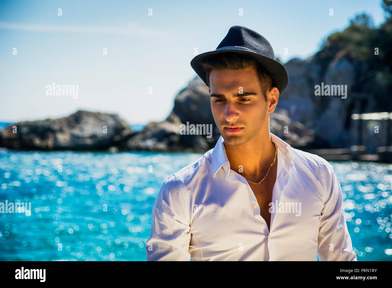Schönen jungen Mann in elegantes weißes Hemd und schwarzen Filzhut, am Strand beim wegschauen. Wellen des Meeres im Hintergrund Stockfoto