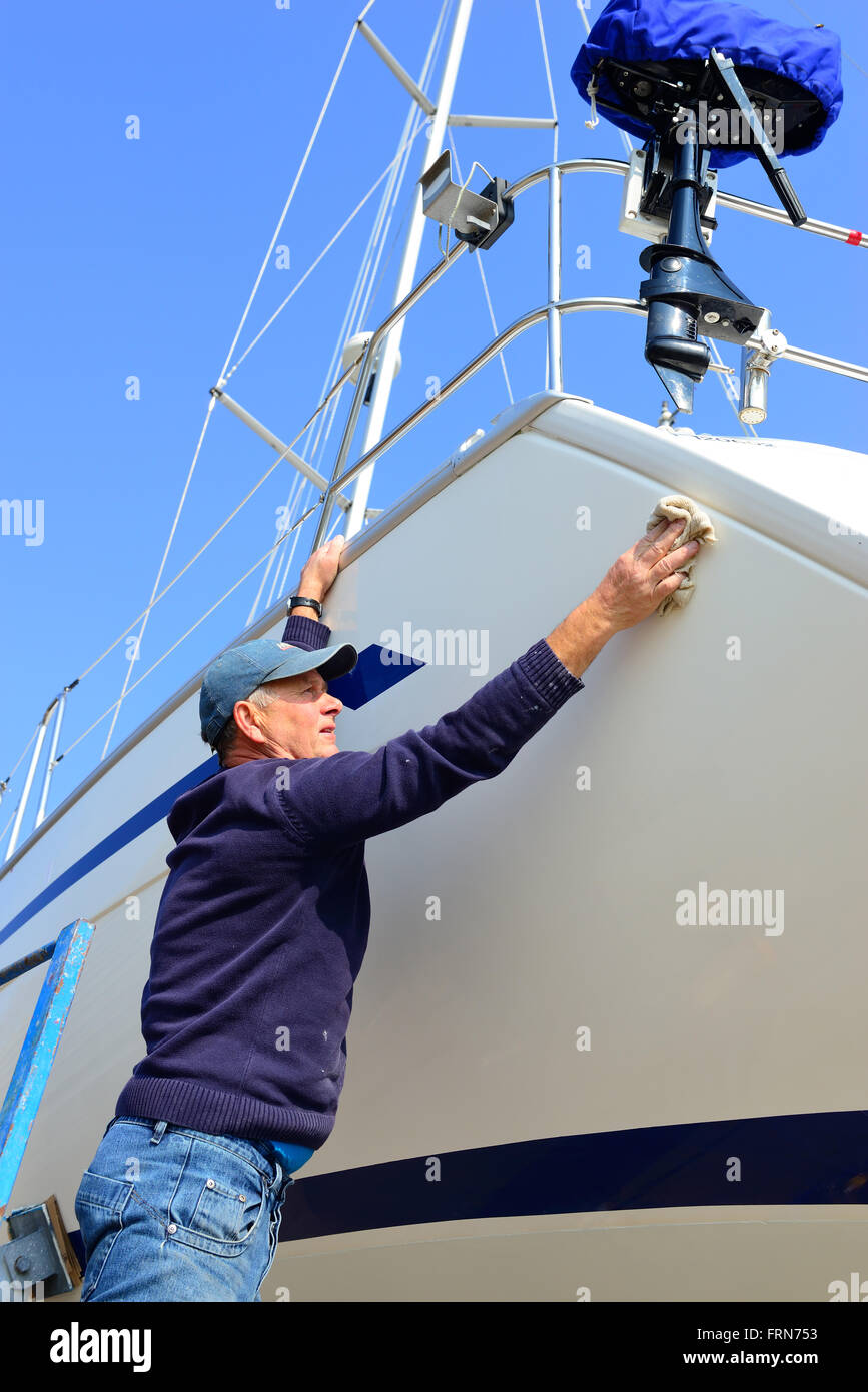 Der Bootsbesitzer poliert zu Beginn der Segelsaison den Rumpf seines Bootes an Land im Jachthafen - Chichester, West Sussex, England, Großbritannien Stockfoto