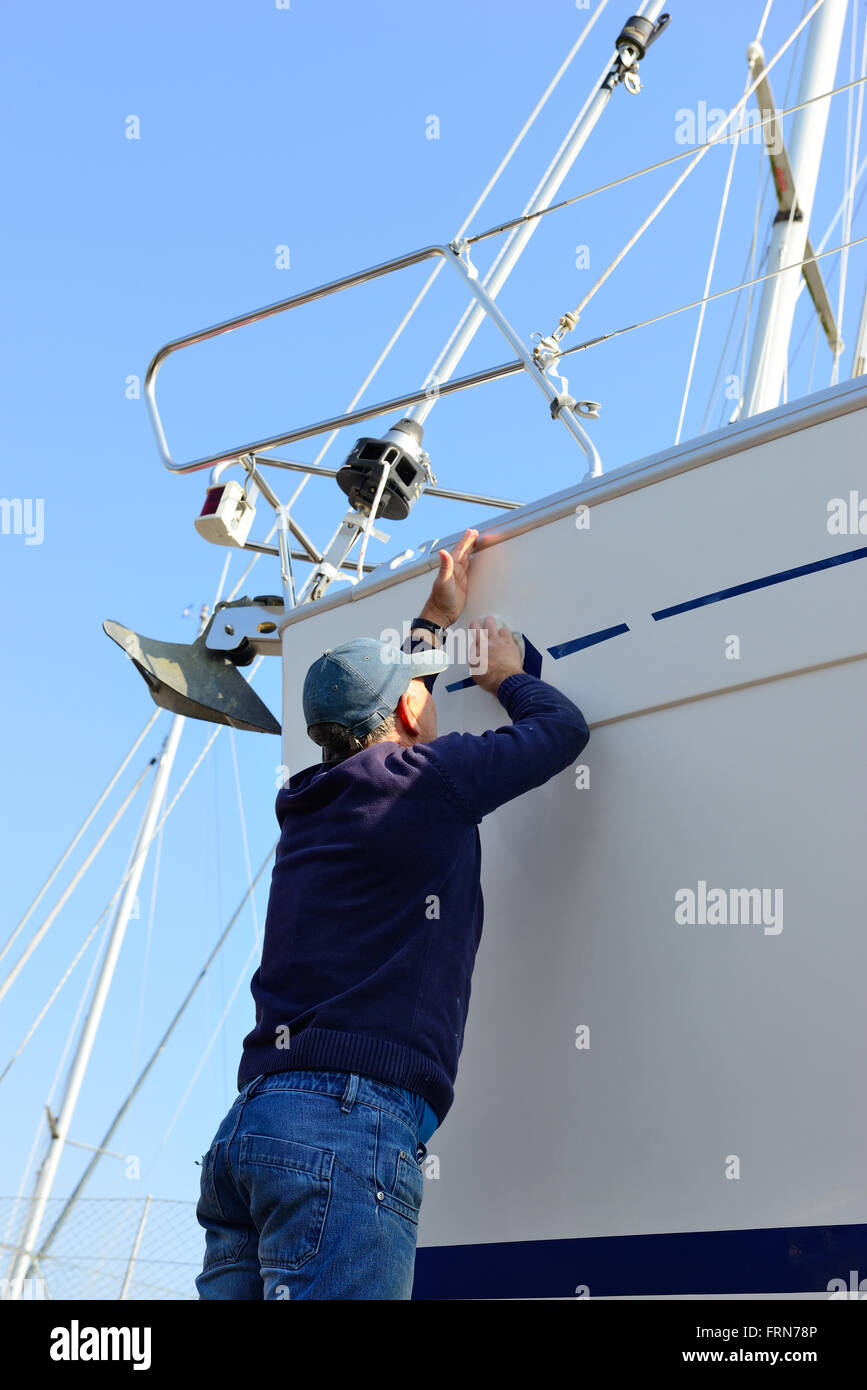 Der Bootsbesitzer poliert zu Beginn der Segelsaison den Rumpf seines Bootes an Land im Jachthafen - Chichester, West Sussex, England, Großbritannien Stockfoto