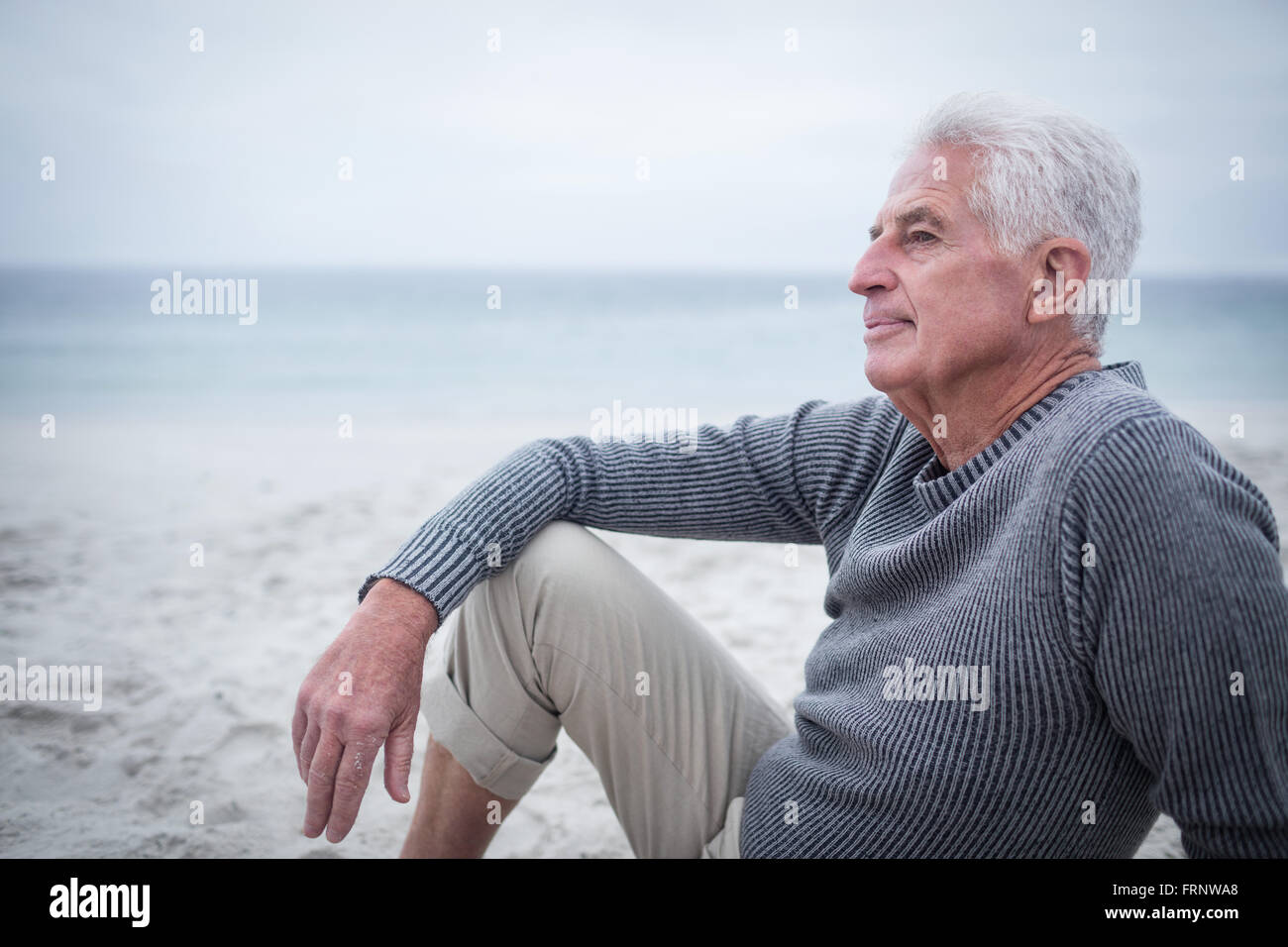 Nachdenklicher pensionierter Mann am Strand sitzen Stockfoto