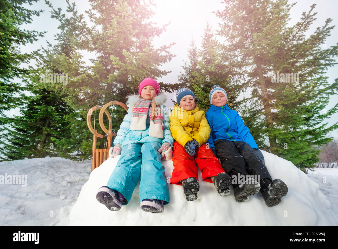 Kleine Kinder sitzen auf Schneewand im park Stockfoto