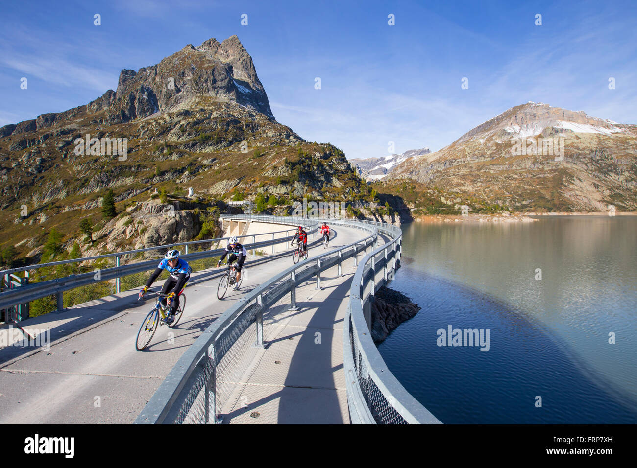 Vier Rennradfahrer auf der Staumauer Emosson-Stausee in den Alpen an der Grenze zwischen Frankreich und der Schweiz. Stockfoto