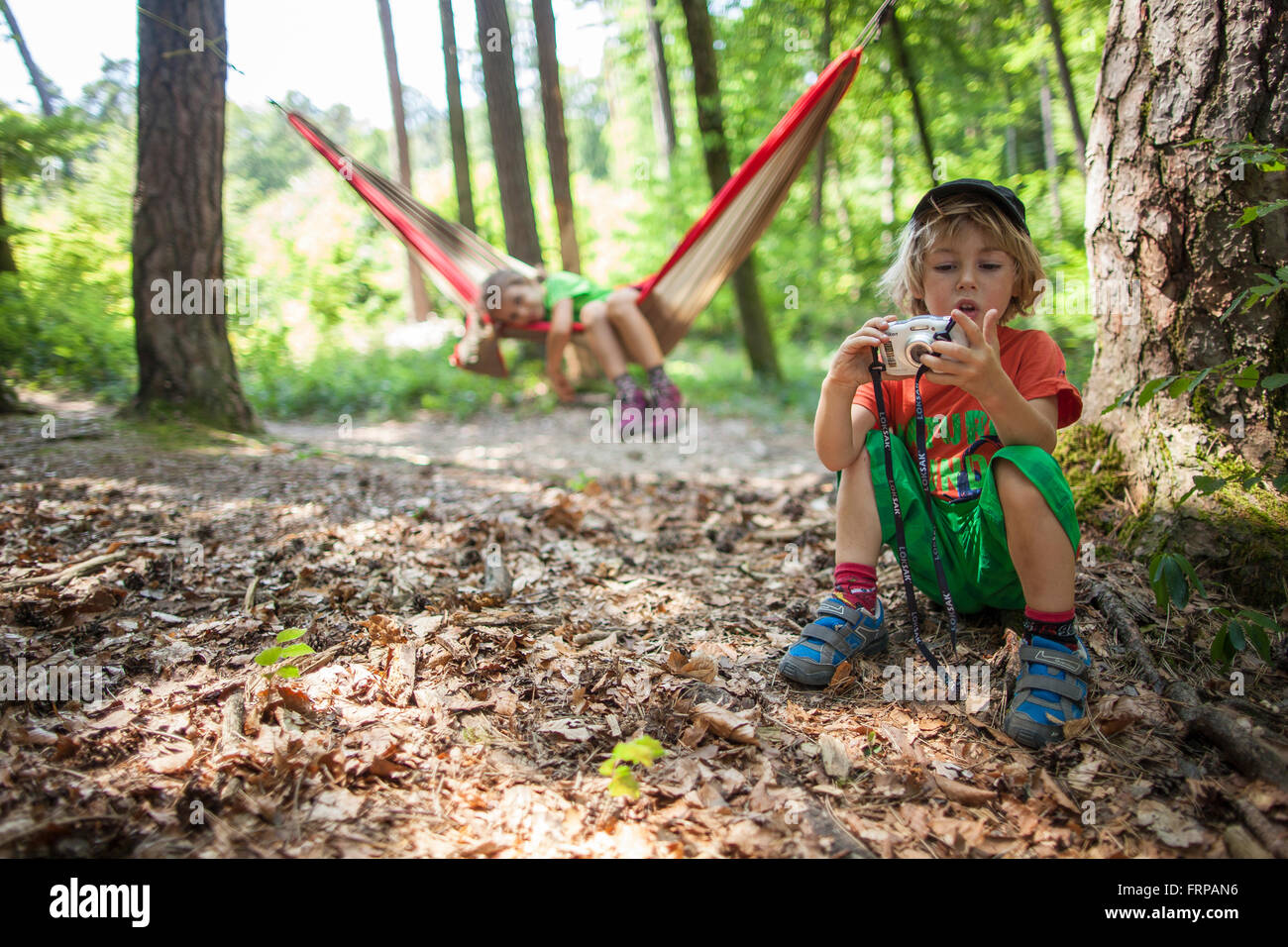Ein 5 Jahre altes Mädchen in einer Hängematte, mit ihrem Bruder spielen mit einer Kamera. In einem Wald, Frankreich. Stockfoto