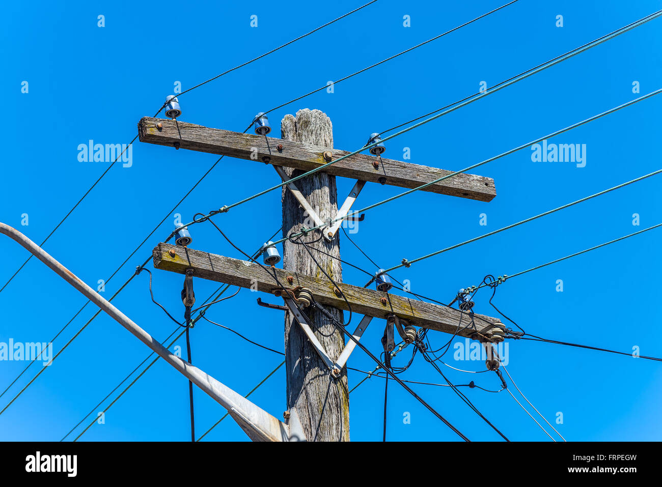 Alte einfache Elektrizität ländlichen hölzernen Strommast mit Kabeln und Isolatoren gegen blauen Himmel Stockfoto